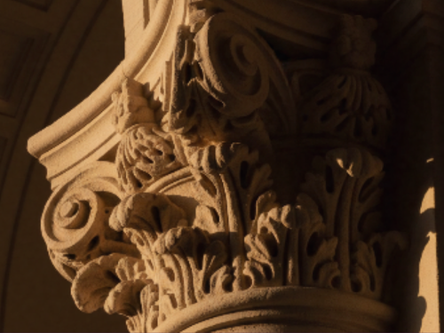 Close-up of an ornate, carved stone Corinthian column capital with acanthus leaf motifs.