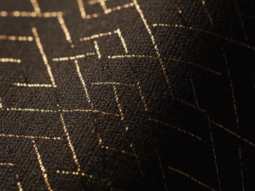 Close-up of black fabric with gold geometric stitching pattern.