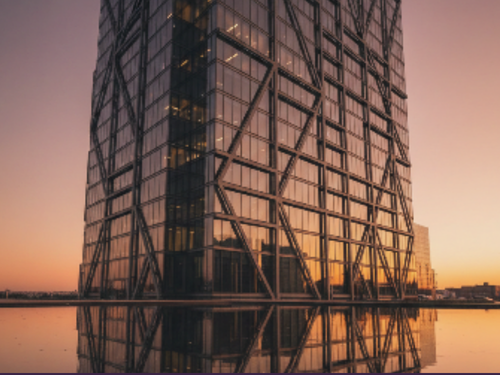 Reflection of a modern glass skyscraper with an intricate metal framework at sunset.