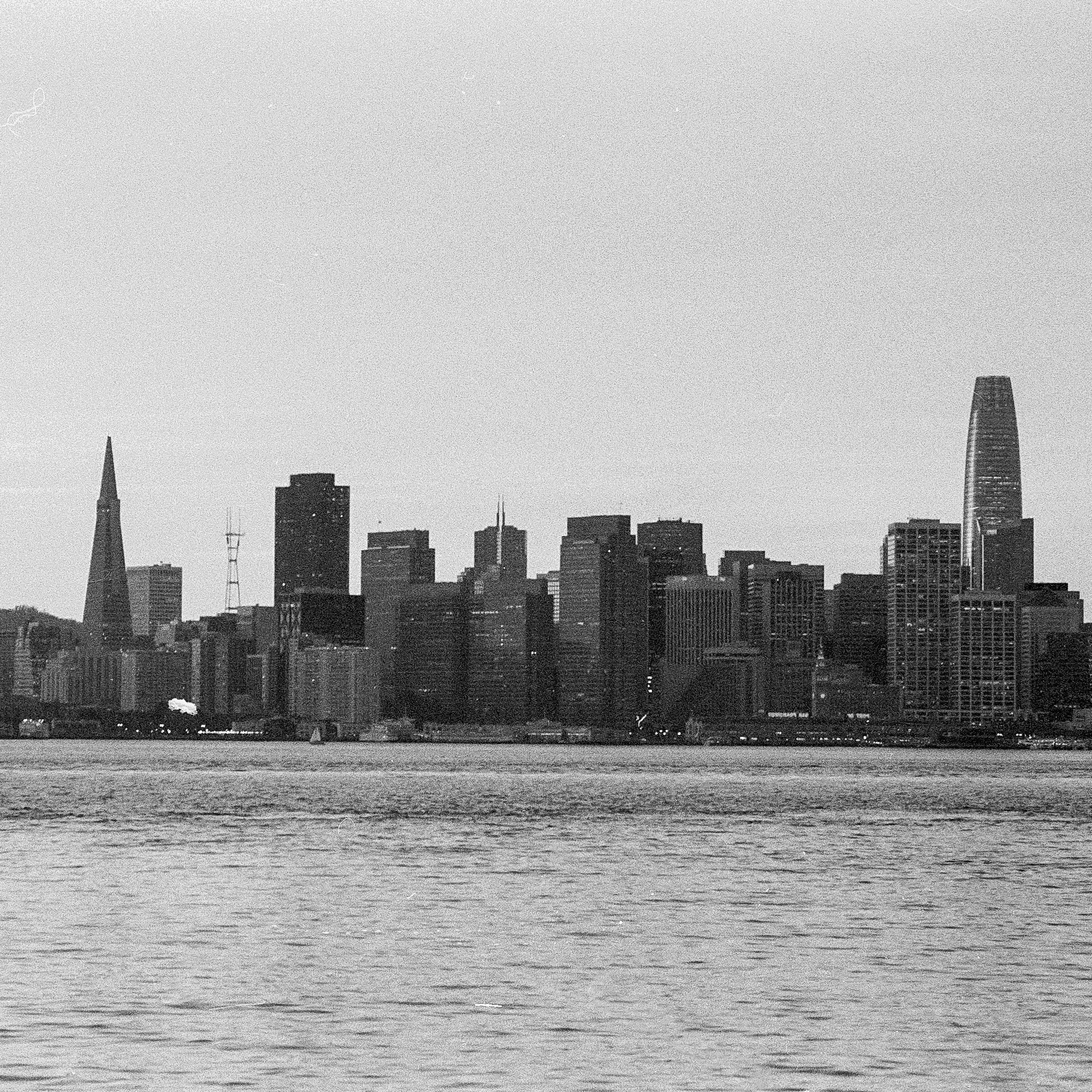 A city skyline with tall buildings and skyscrapers viewed across a body of water on a clear day.