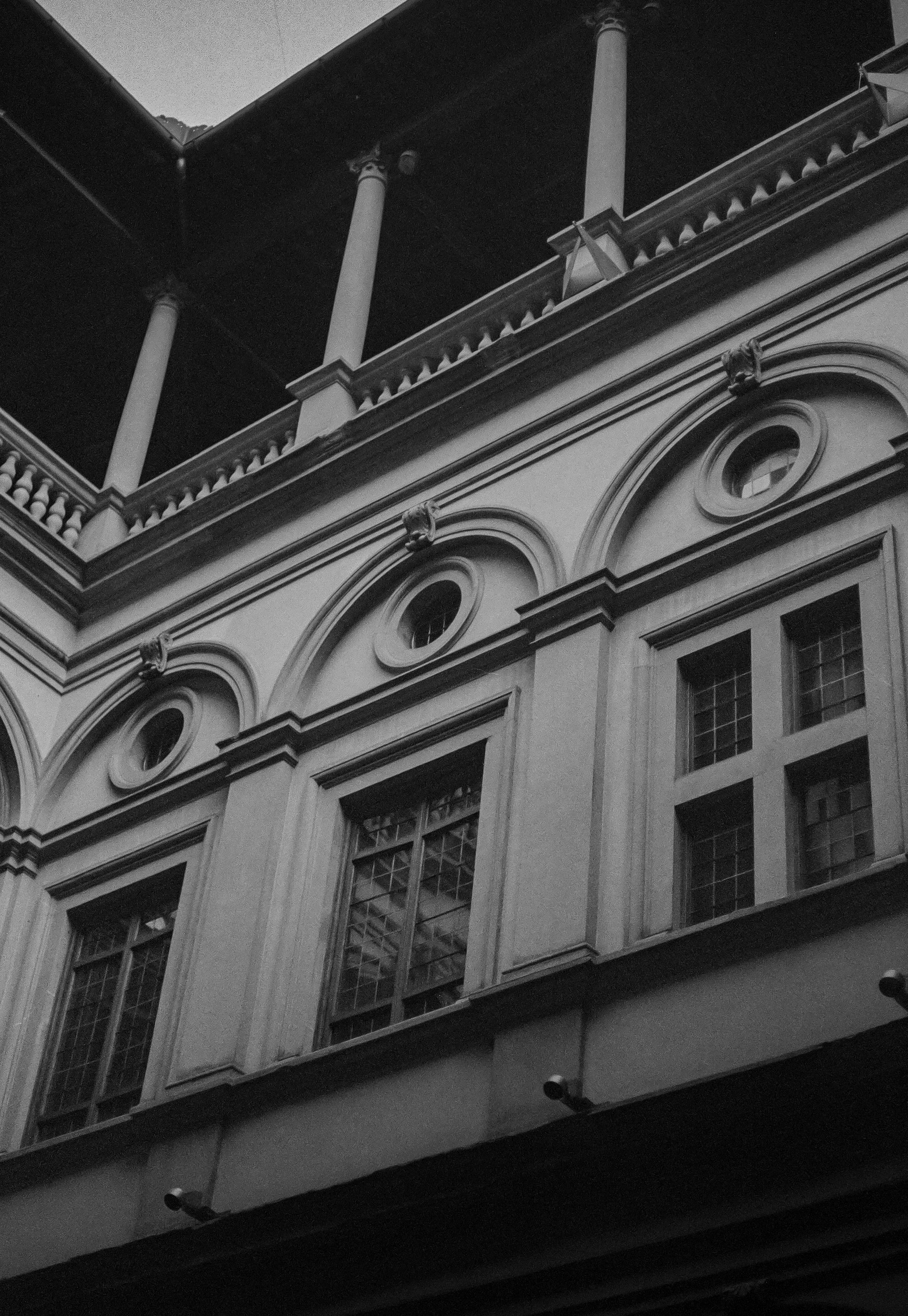 Black and white photograph of an ornate building facade with arched windows and decorative columns, viewed from below against a dark sky.