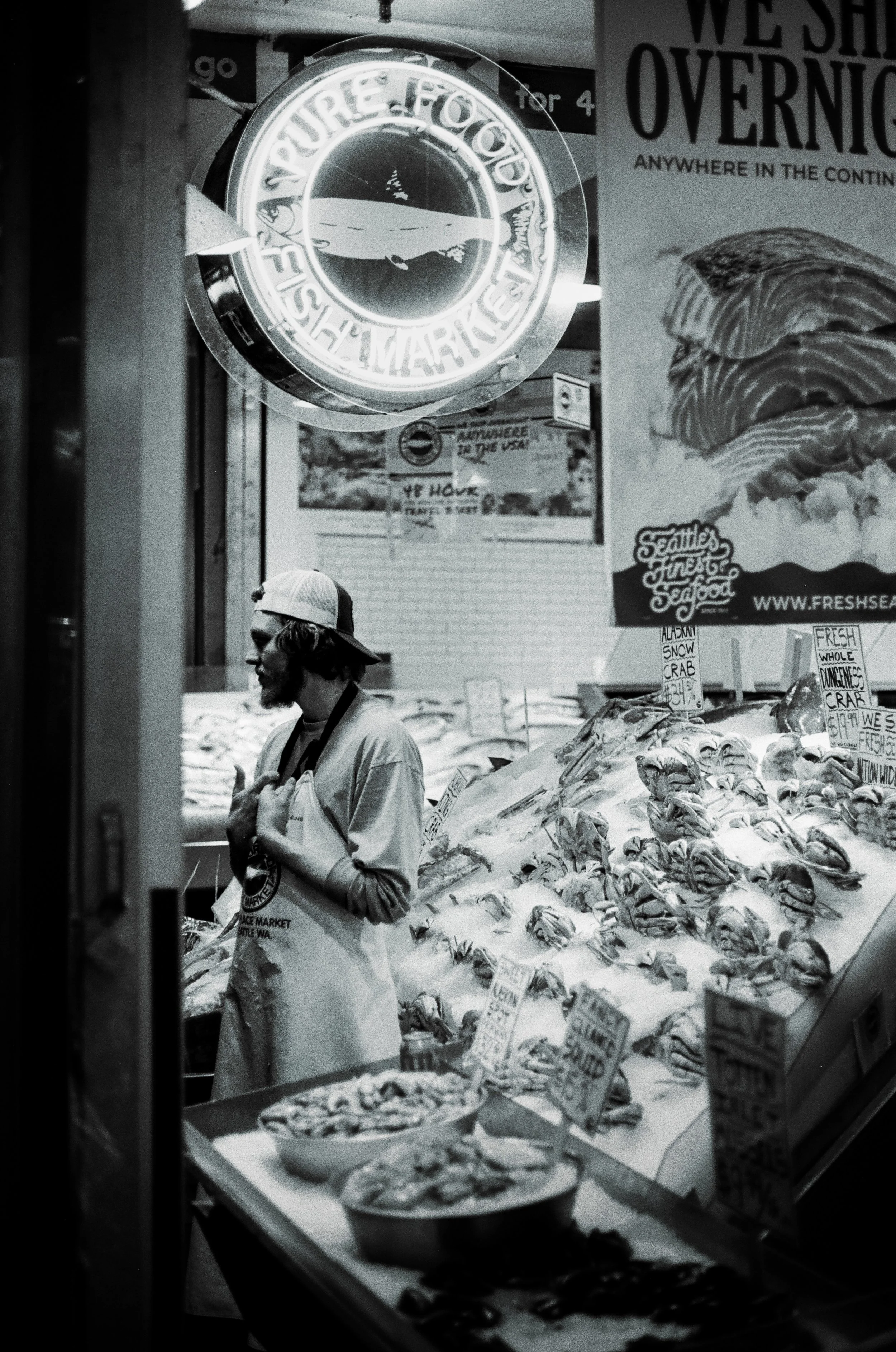 A person shopping at a seafood market, standing in front of a display piled high with fresh fish and seafood, with signs indicating prices and types of seafood.