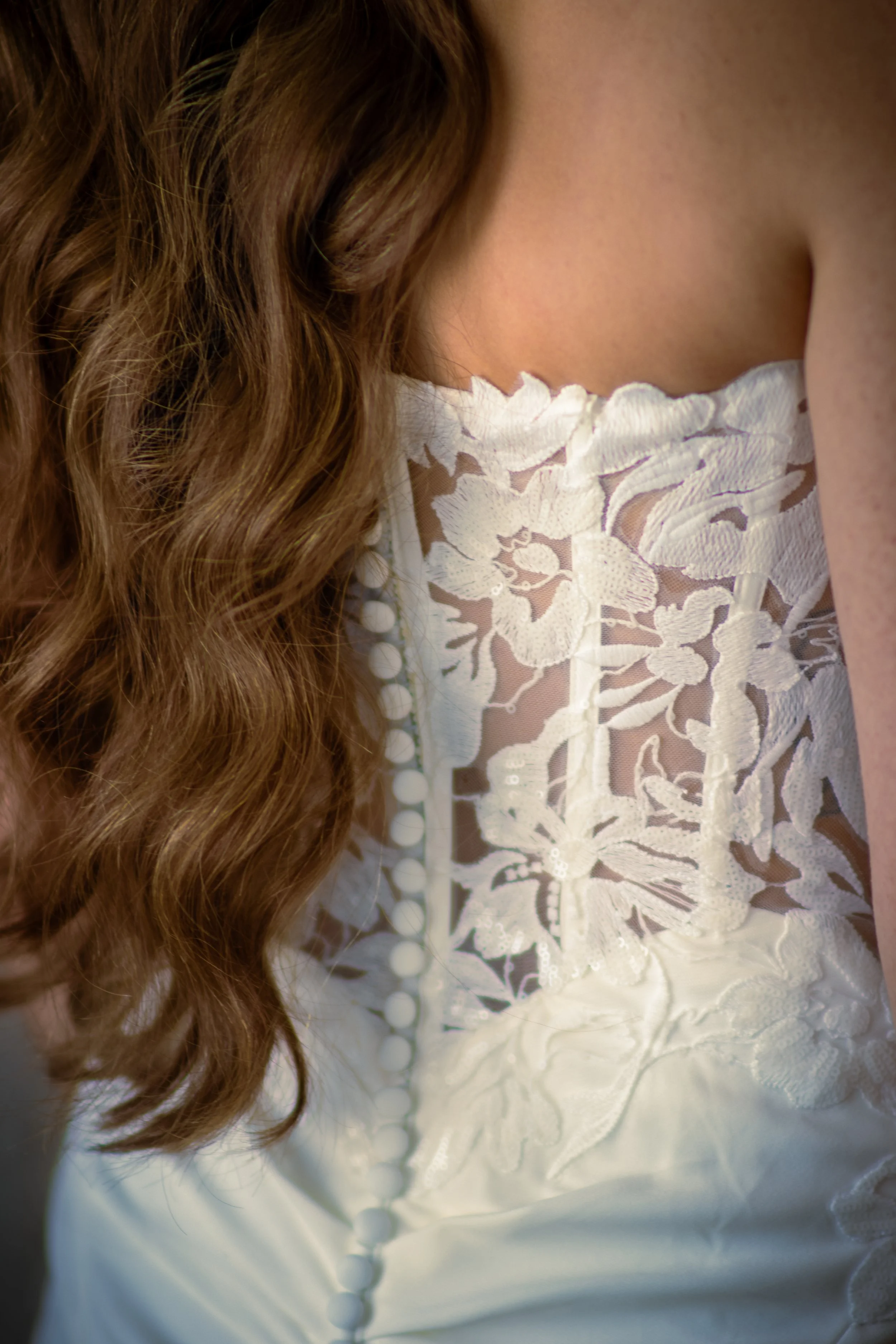 Close-up of a woman in a white lace top with curly brown hair.