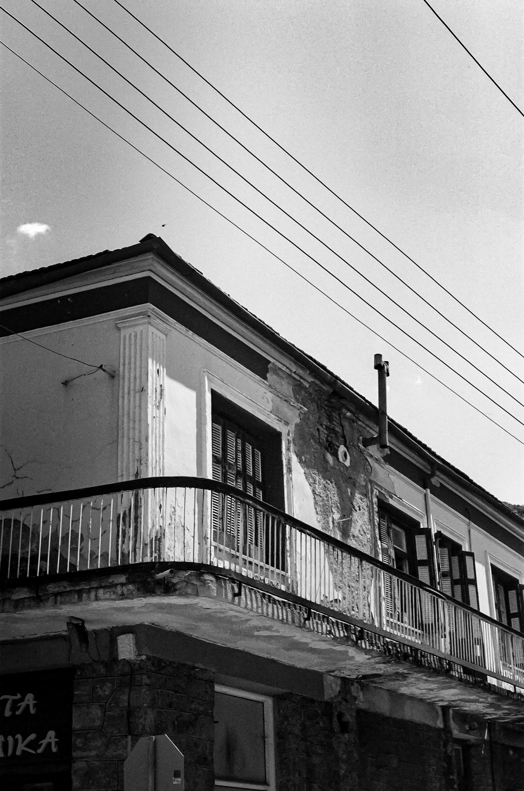 Black and white photo of a building with a balcony, neighboring building, and electrical wires in the sky.