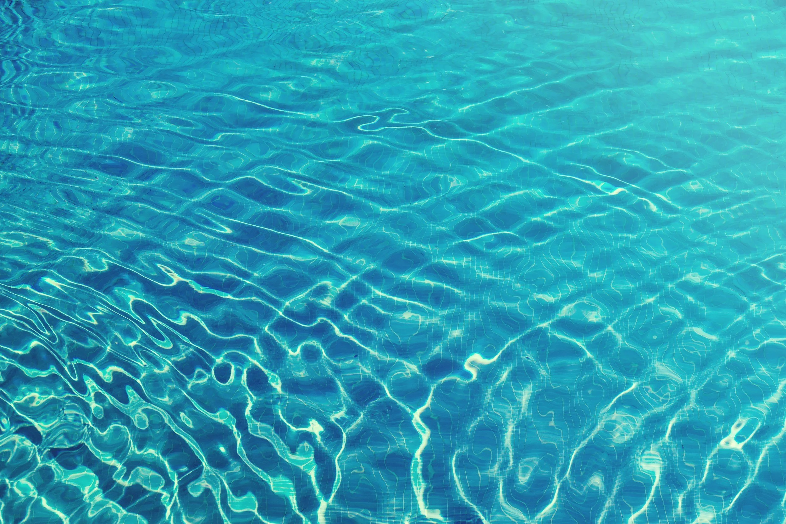 Close-up of a swimming pool's water surface showing ripples and light reflections.
