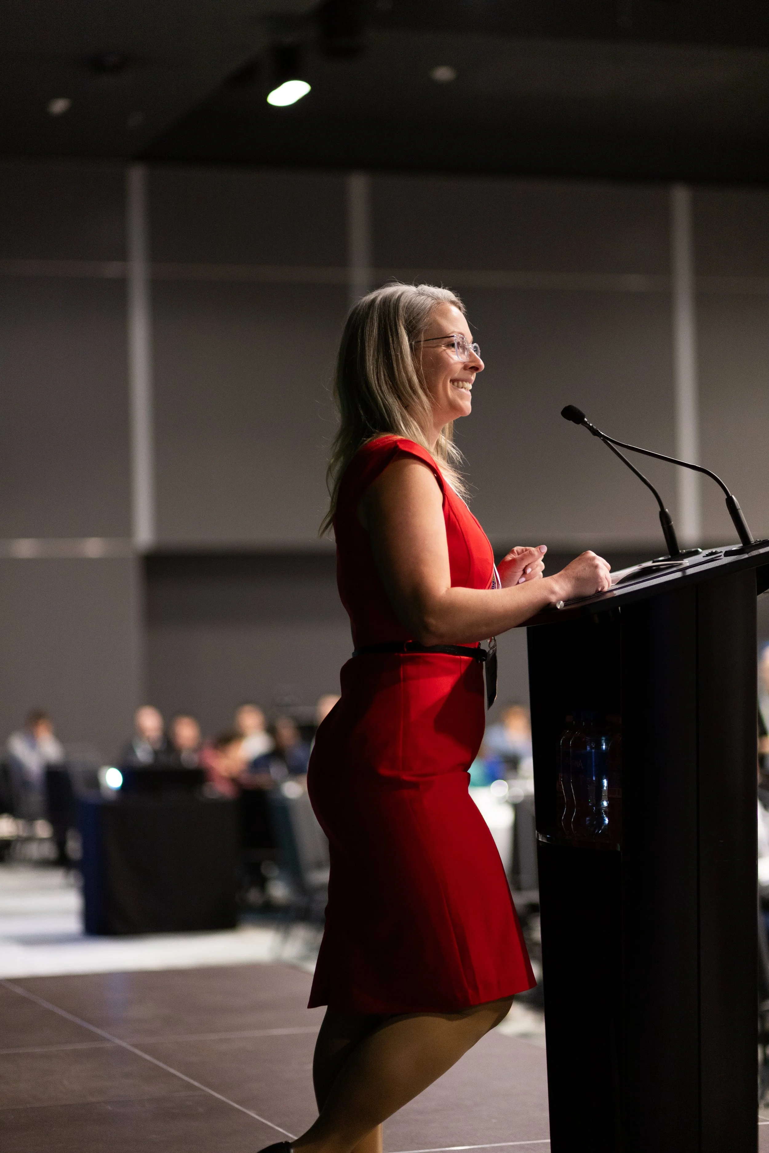 A woman in a red dress speaking at a podium at a conference.