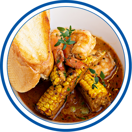 New Orleans seafood corn bisque with corn on the cob, shrimp, and herbs, served with toasted bread.