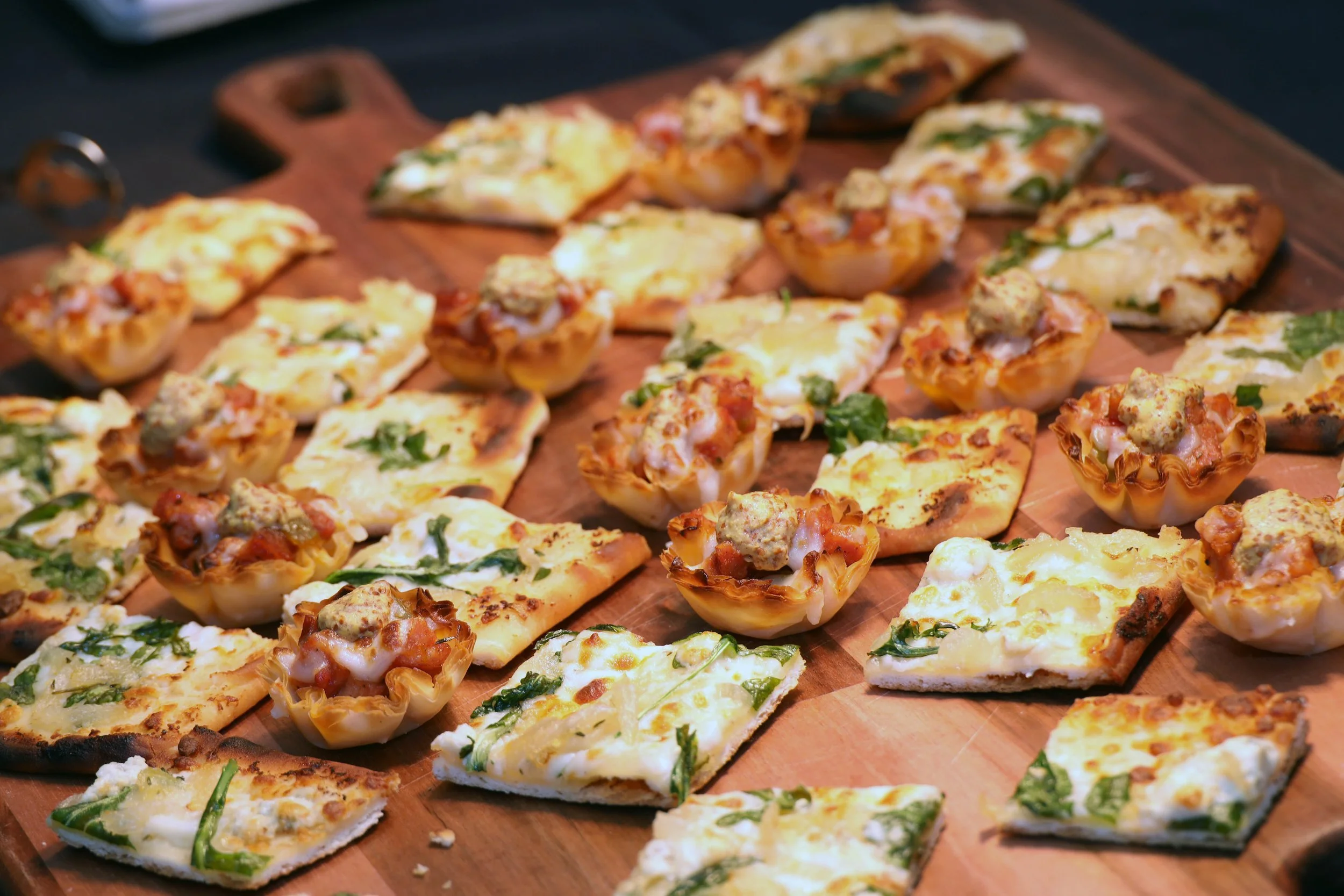 Assorted mini pizzas and stuffed bread on a wooden board.