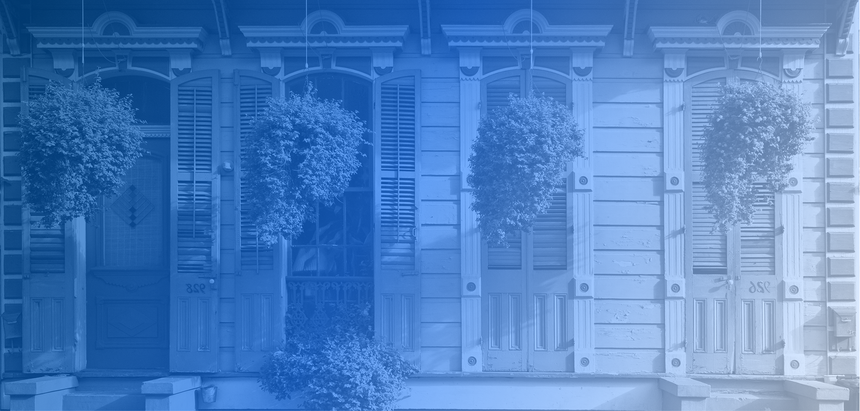 Front view of a New Orleans house with wooden shutters, and potted plants in front.