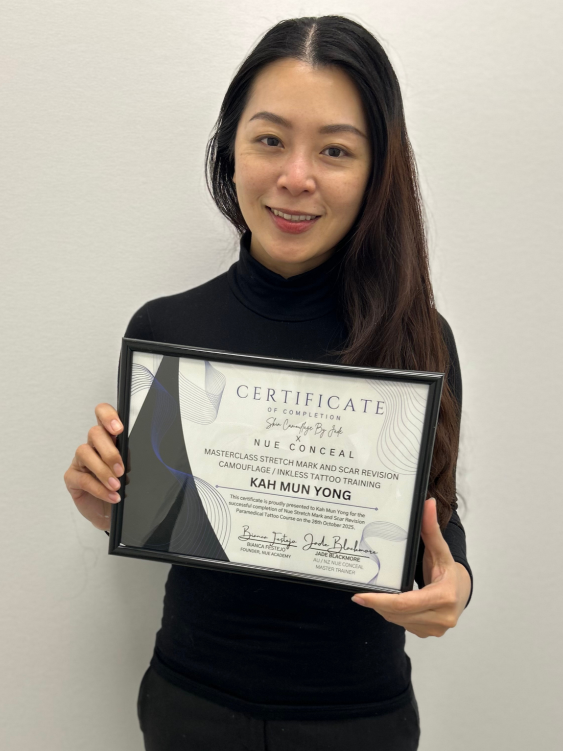 Woman smiling and holding a framed certificate for paramedical tattoo training.