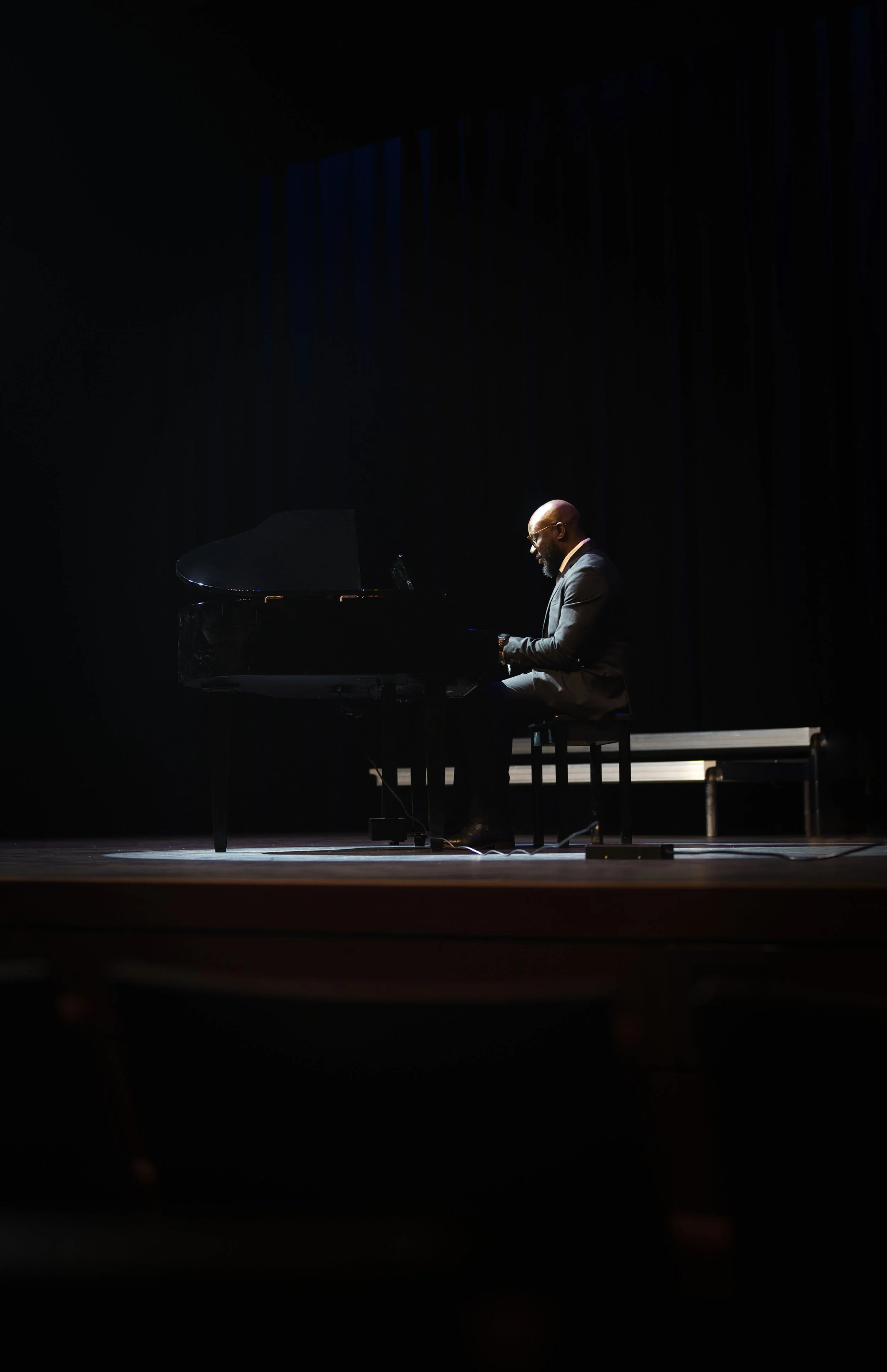 Man in a suit playing a grand piano on a dimly lit stage.