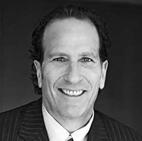 Black and white headshot of a smiling man with curly hair, wearing a suit and tie.