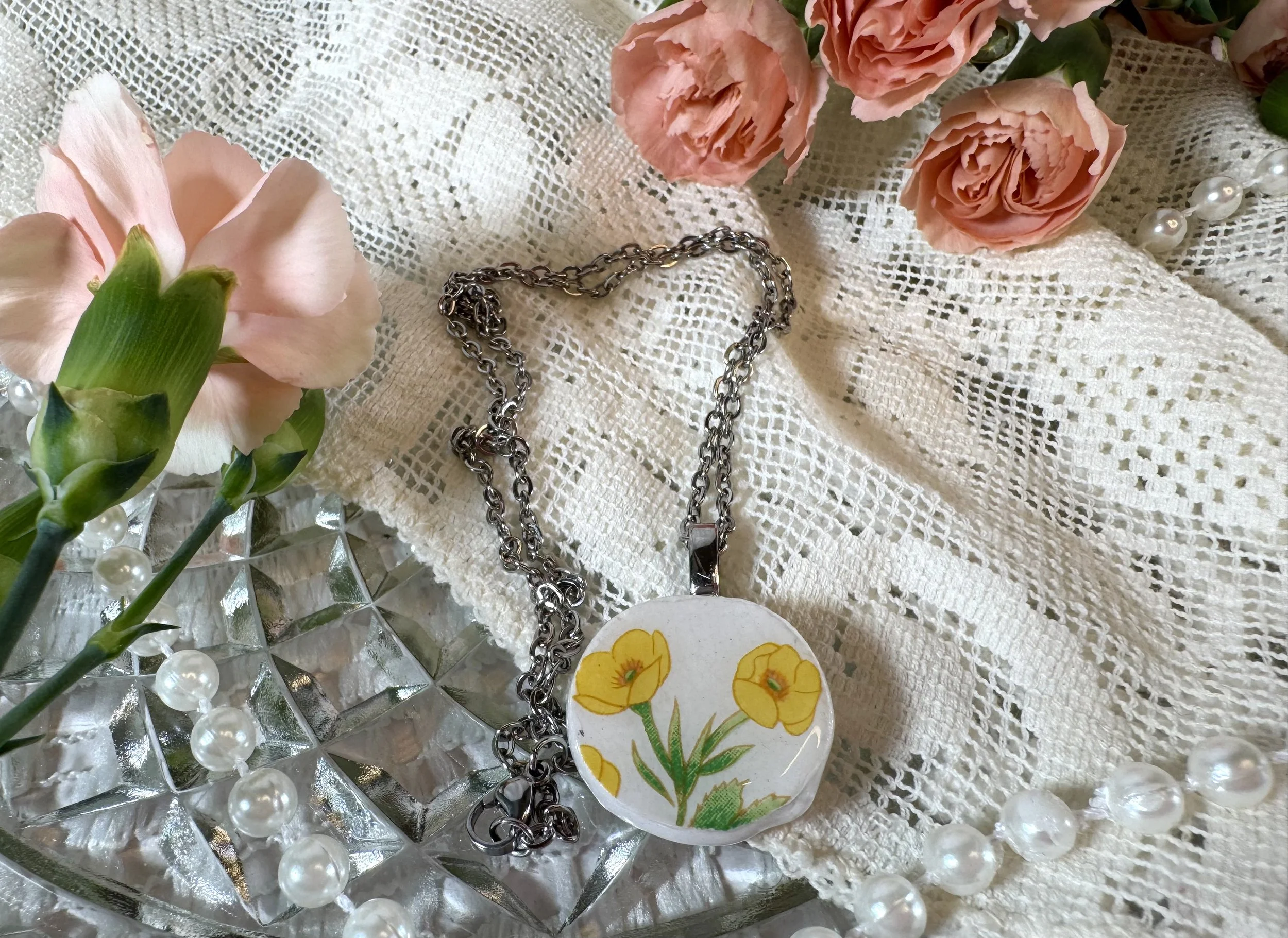 A lace fabric tablecloth with peach roses, a string of pearls, a metallic chain, a decorative dish with a floral design, and a crystal tray.