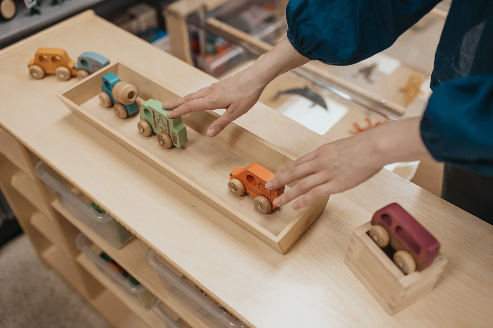Person arranging colored wooden toy trains on a wooden table with a box to hold them.