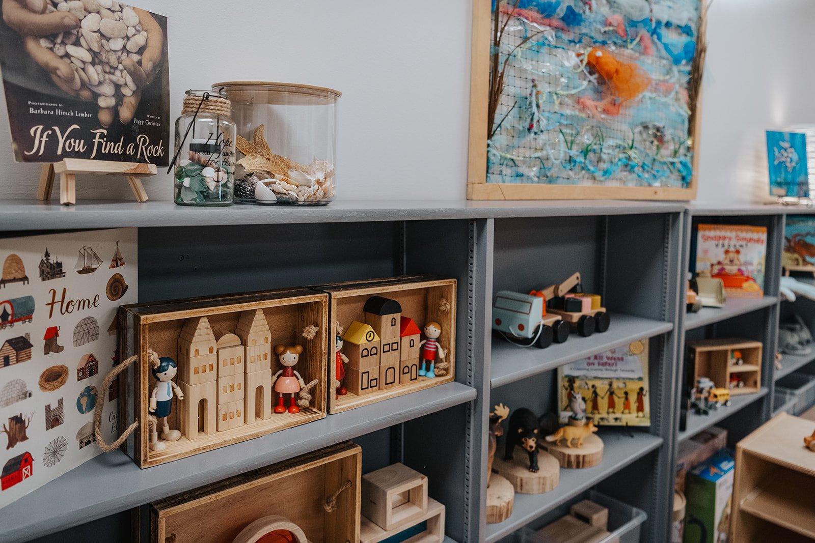 Shelves displaying various handmade crafts and toys, including wooden houses, figurines, and decorative items, in a store or craft shop.