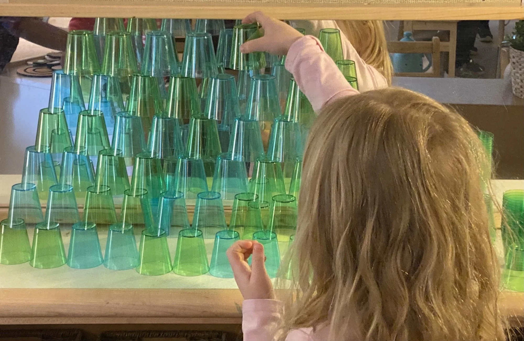 Children playing a game of stacking colorful plastic cups in a pyramid shape.