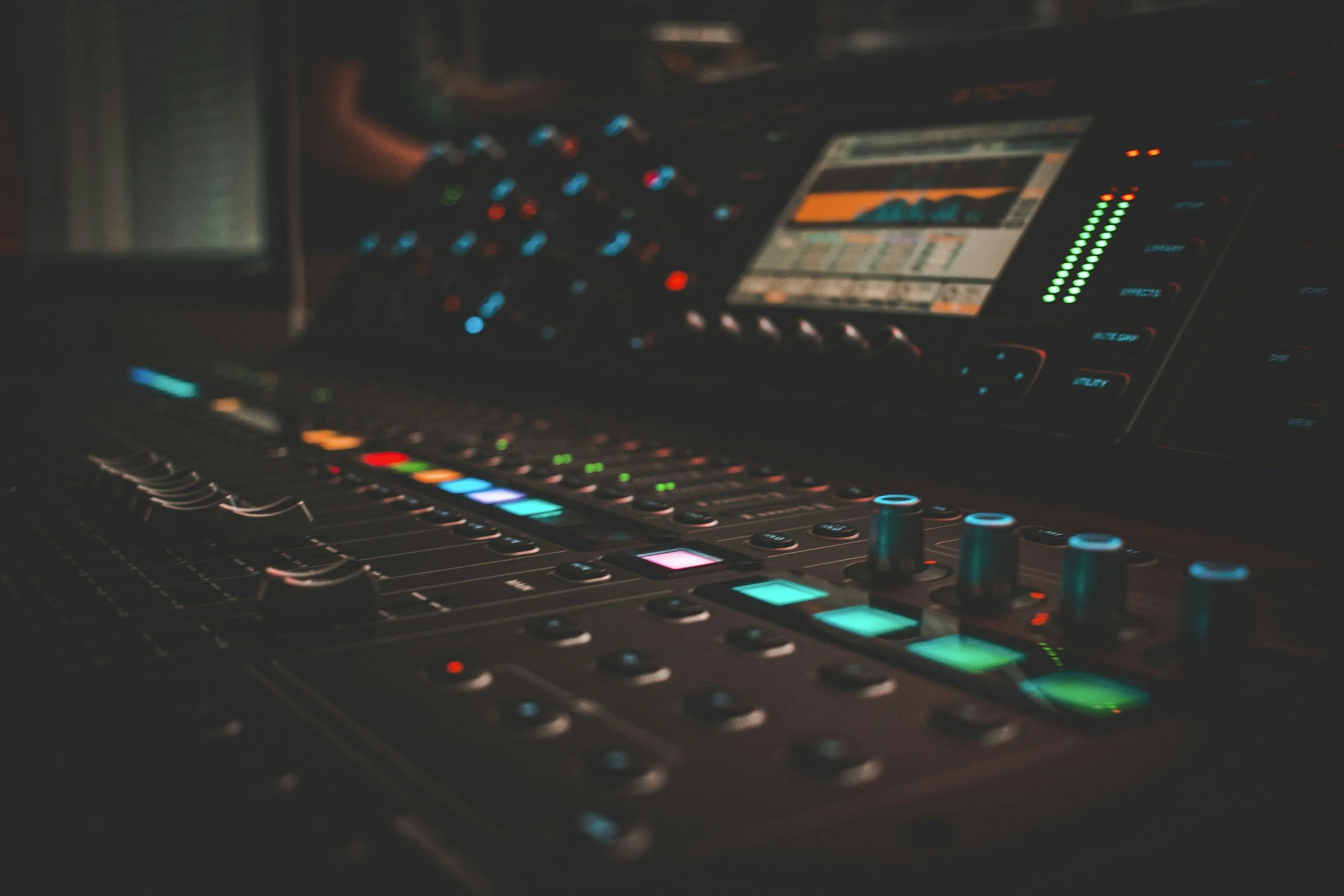 A close-up of a professional DJ mixing console with illuminated controls and a digital screen showing audio levels and waveforms, in a dark setting.