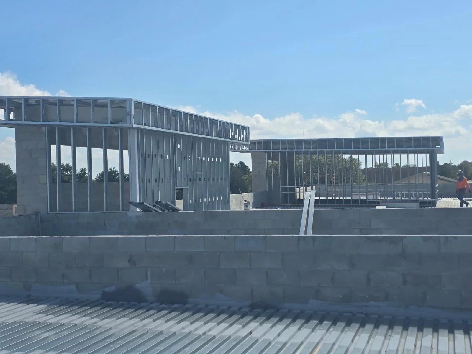 Construction site with steel framing and concrete blocks, workers installing the structure under a partly cloudy sky.
