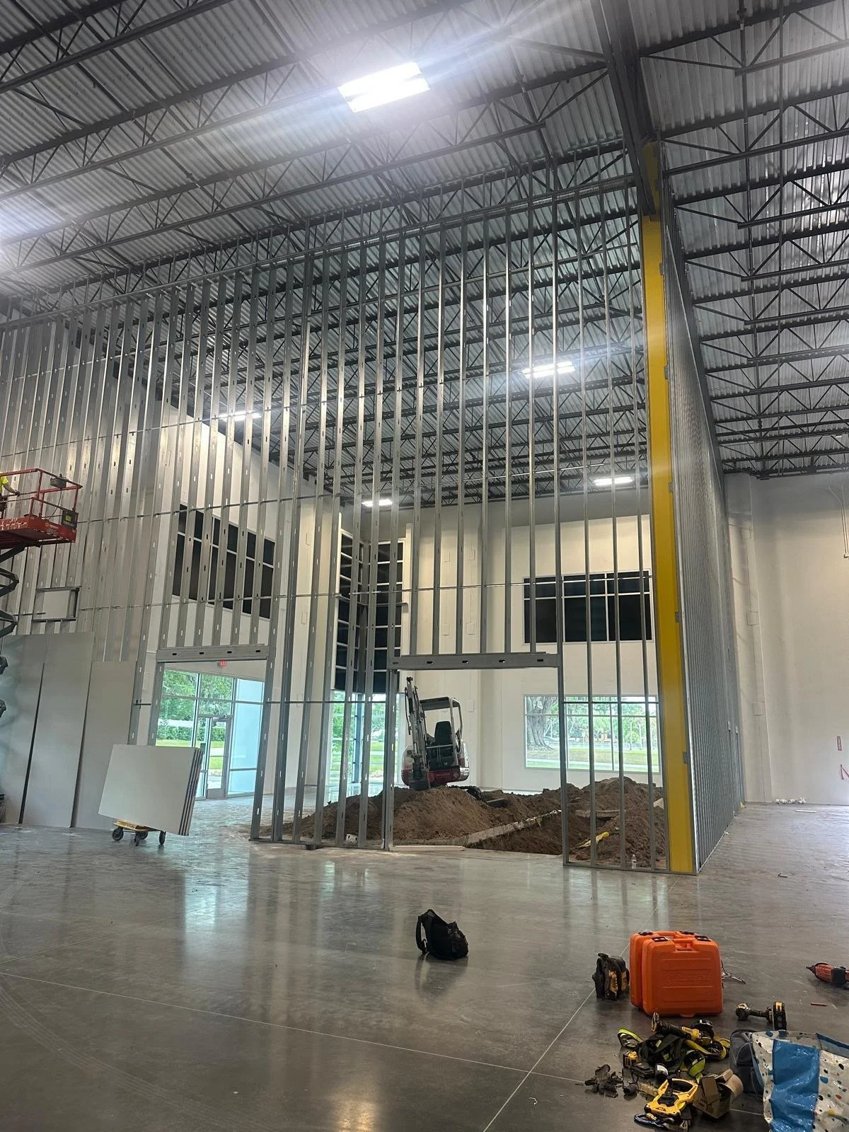 Interior of a building under construction with exposed metal framing, a small construction excavator, and tools on the floor.
