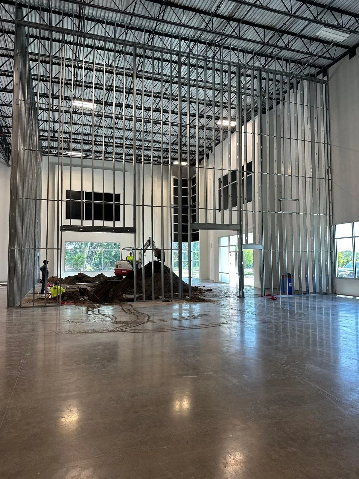Construction workers and equipment inside a building under construction, with metal framing and a dirt pile.