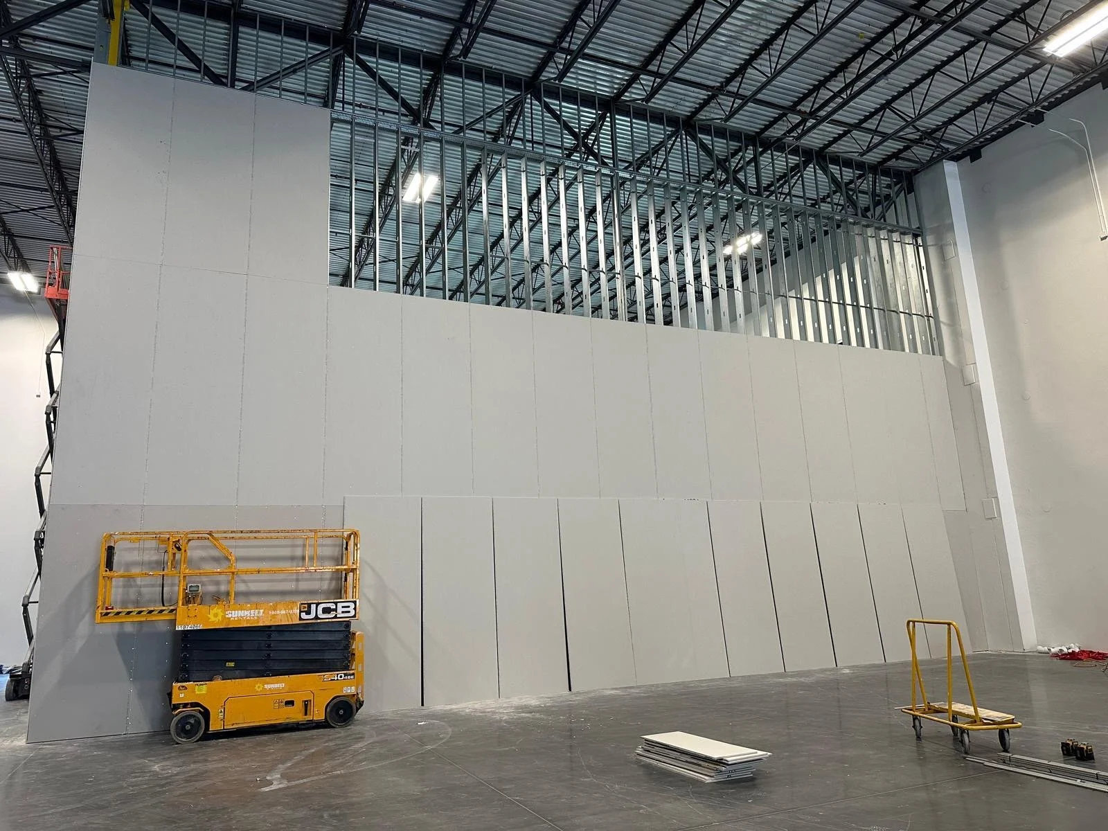 Interior of a building under construction with a large white wall, construction lift, and scaffolding.