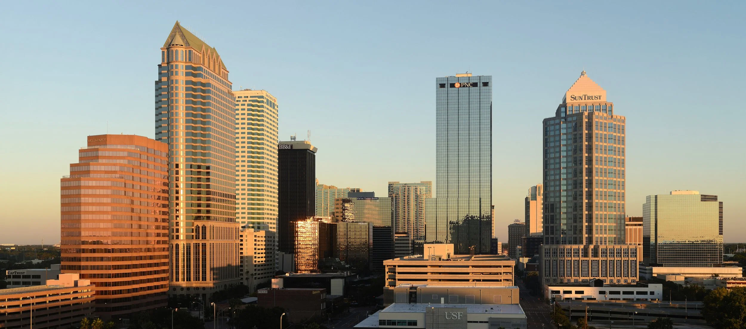 Sunset view of a city skyline with tall modern buildings, including Wells Fargo, BB&T, PNC, and SunTrust, reflecting the setting sun.
