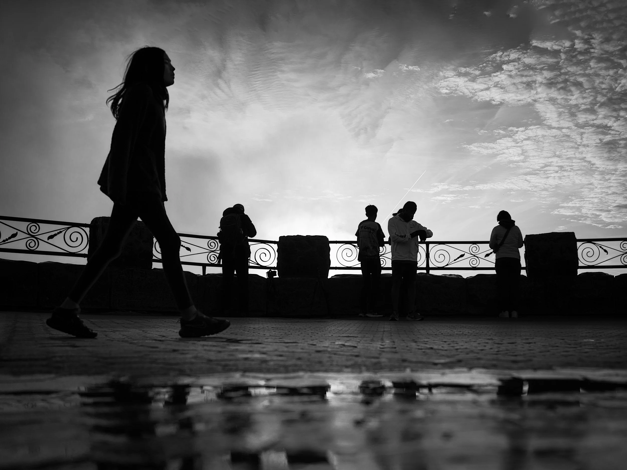 Silhouette of a person walking with others in the background against a cloudy sky during sunset.