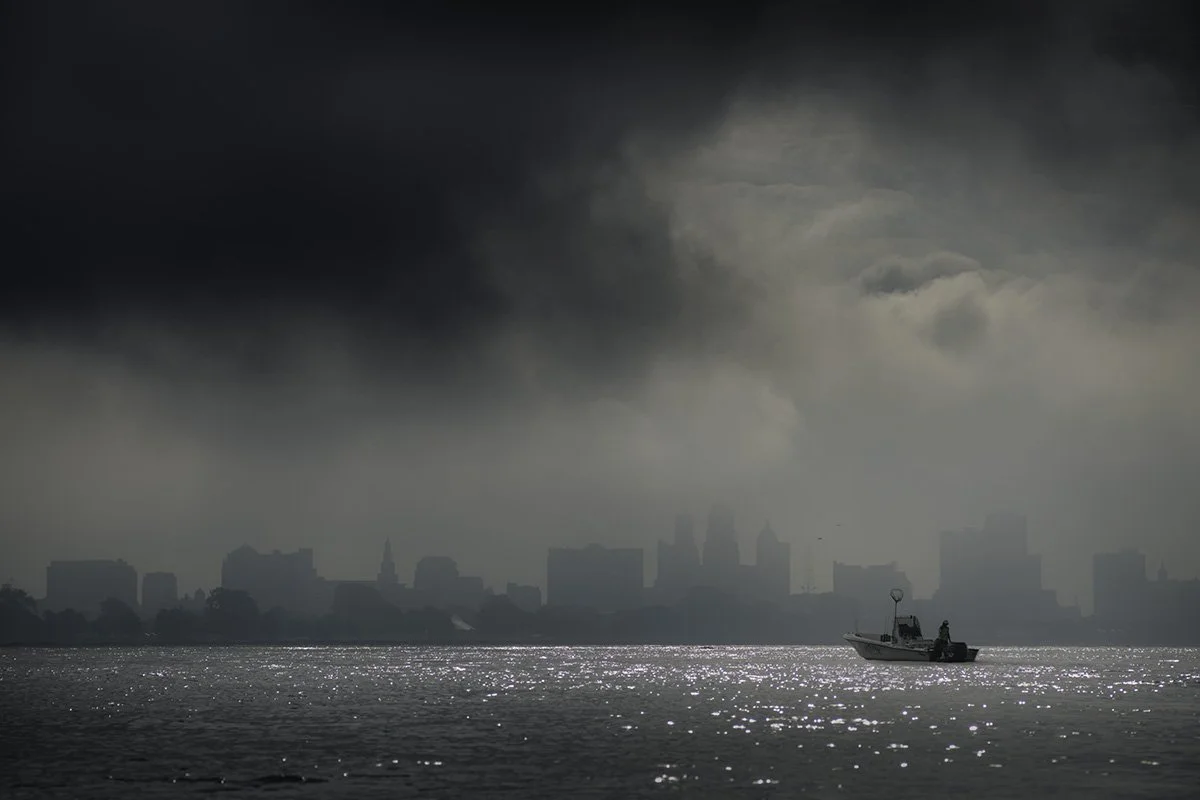 A boat on a body of water with a city skyline and dark storm clouds overhead.