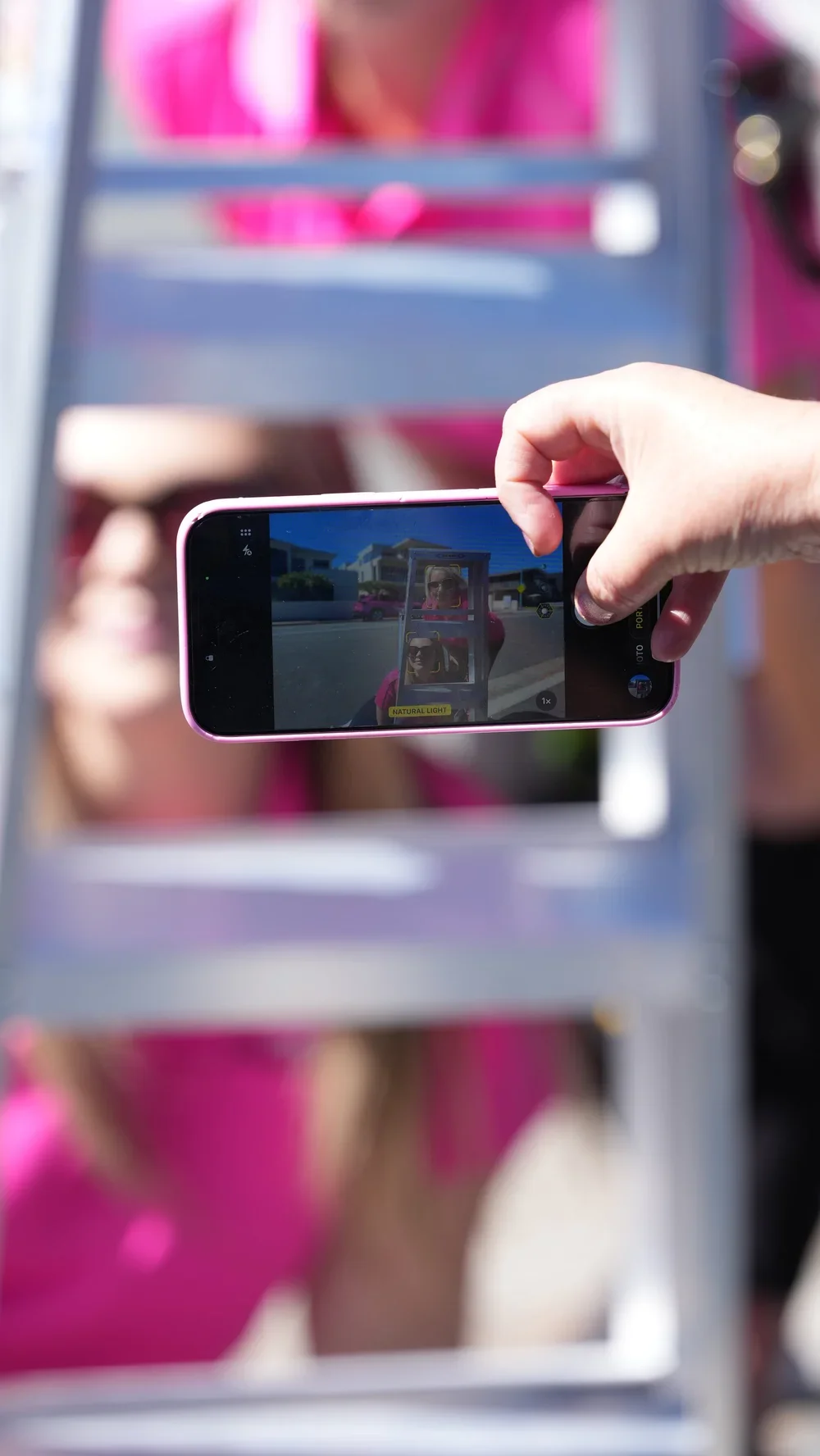 Person taking a photo with a smartphone of a ladders, with the background blurred and wearing a pink shirt.