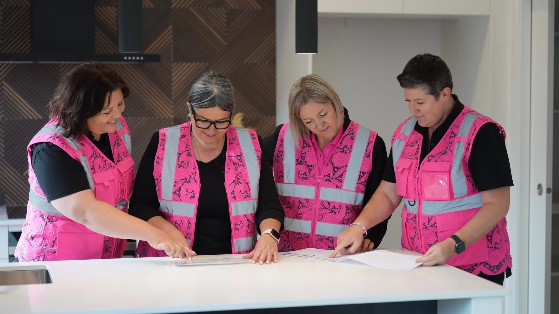 Four people wearing pink safety vests gathered around a table looking at papers.