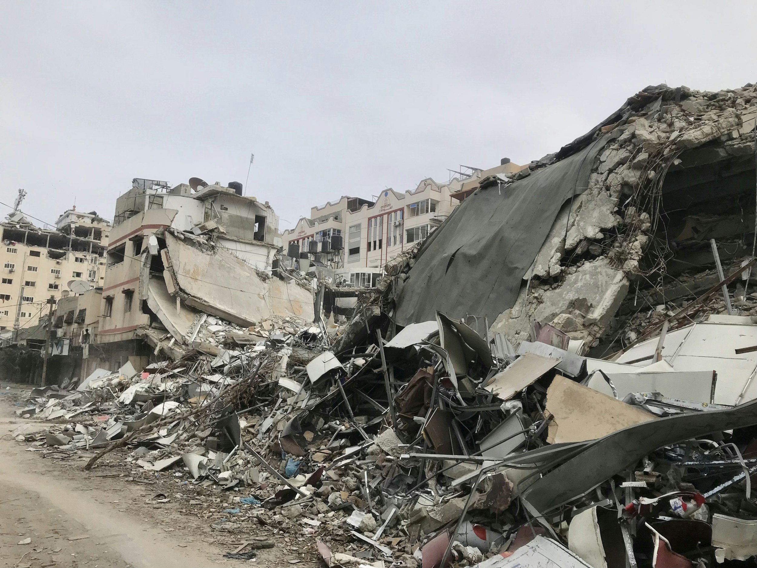 Collapsed buildings with debris and rubble after destruction, possibly due to an earthquake or explosion, with a cloudy sky overhead.