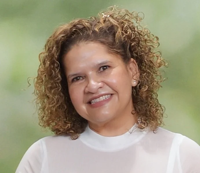A woman with shoulder-length curly hair smiling at the camera against a green background.