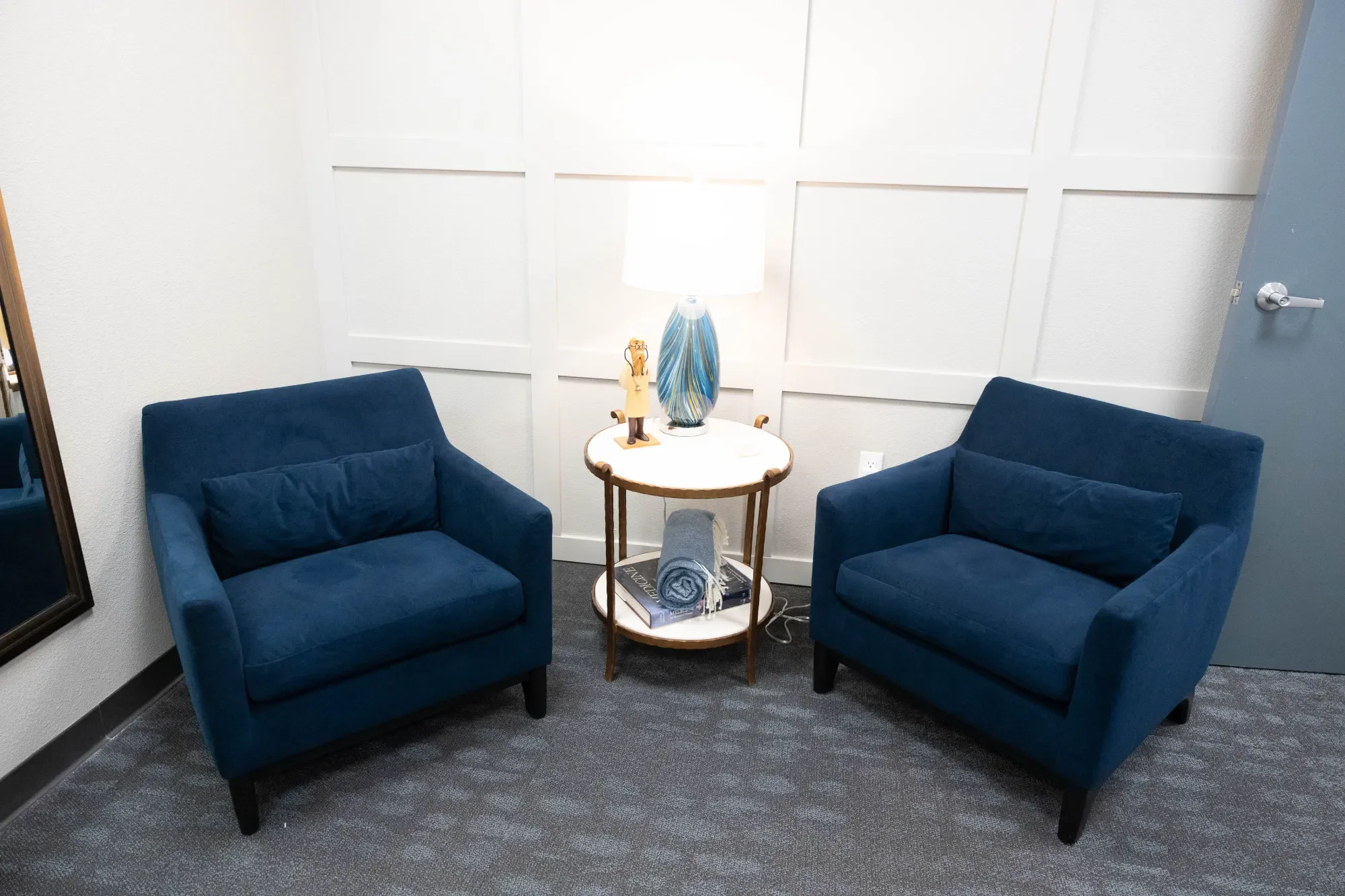 Concierge doctor waiting room with two blue upholstered armchairs facing each other and a round white side table between them
