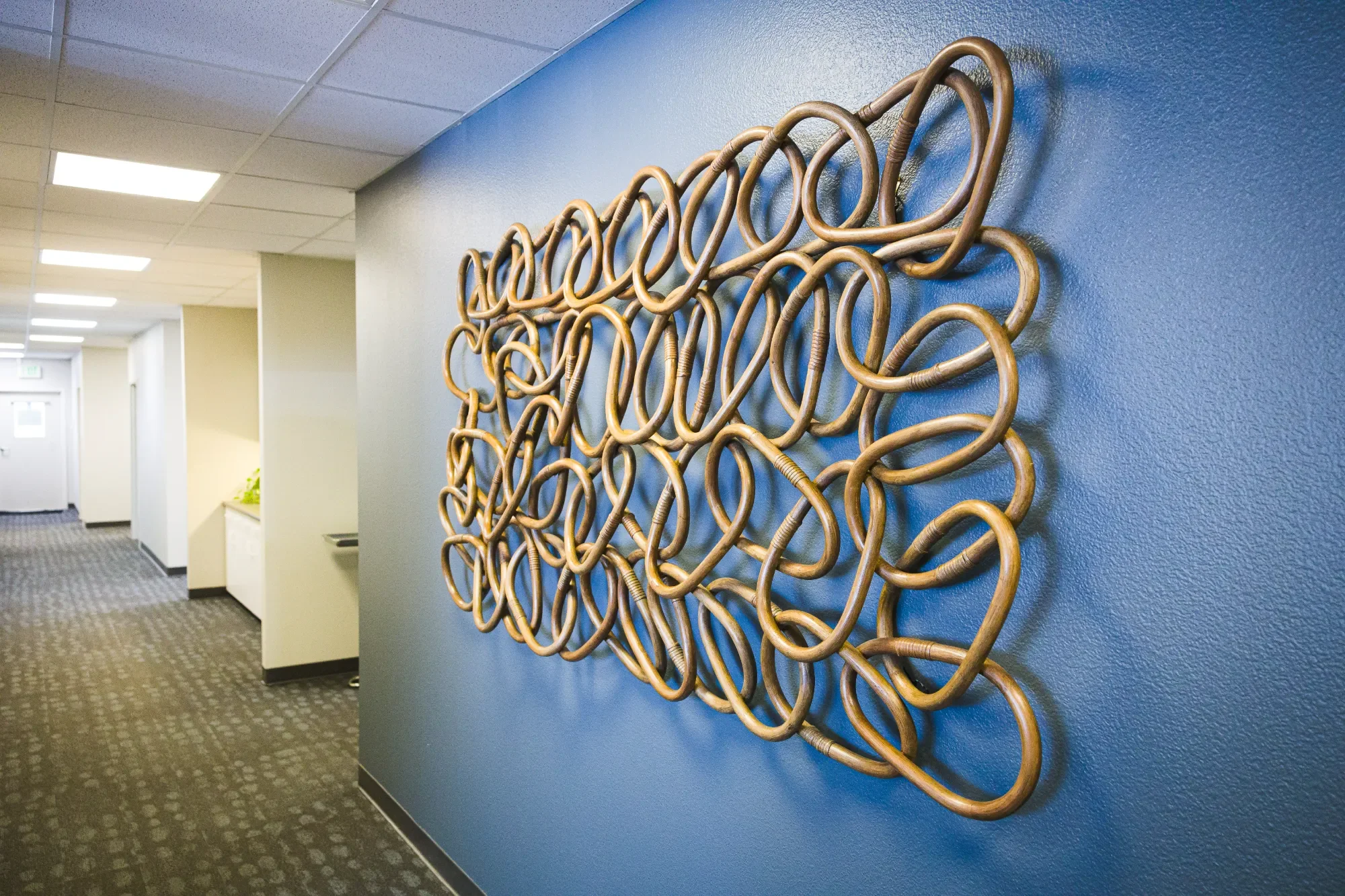 Decorative gold metal artwork mounted on a blue wall in the hallway of medical office
