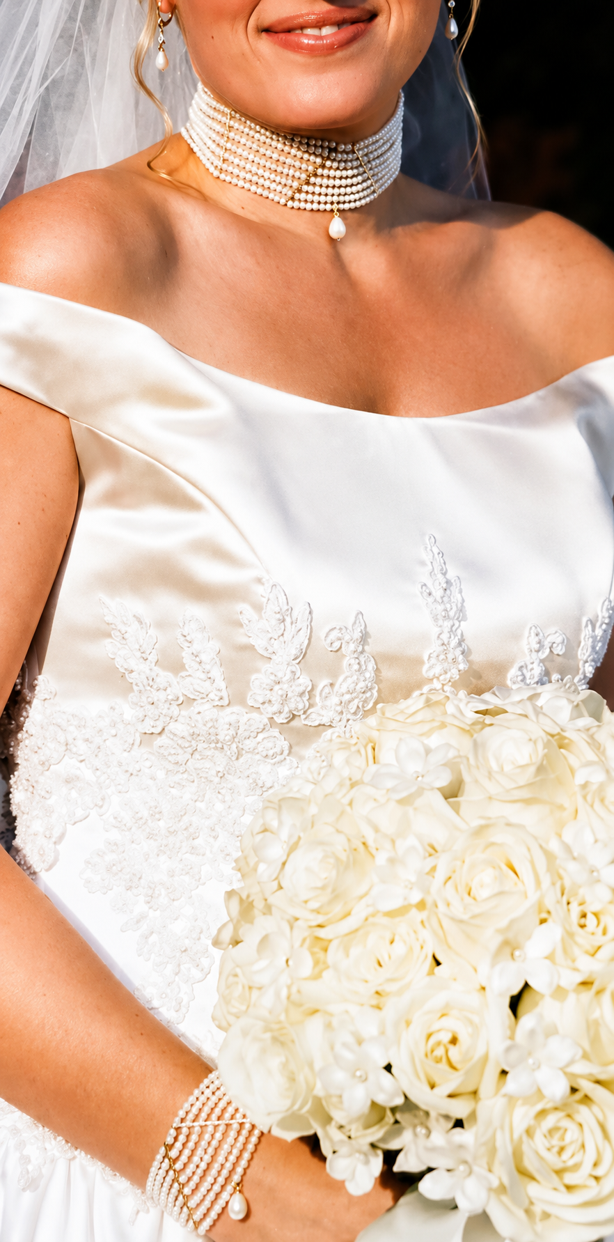 Close-up of a bride in a white satin wedding dress holding a bouquet of white roses and wearing a layered pearl choker necklace, wedding earrings, and pearl bracelet.