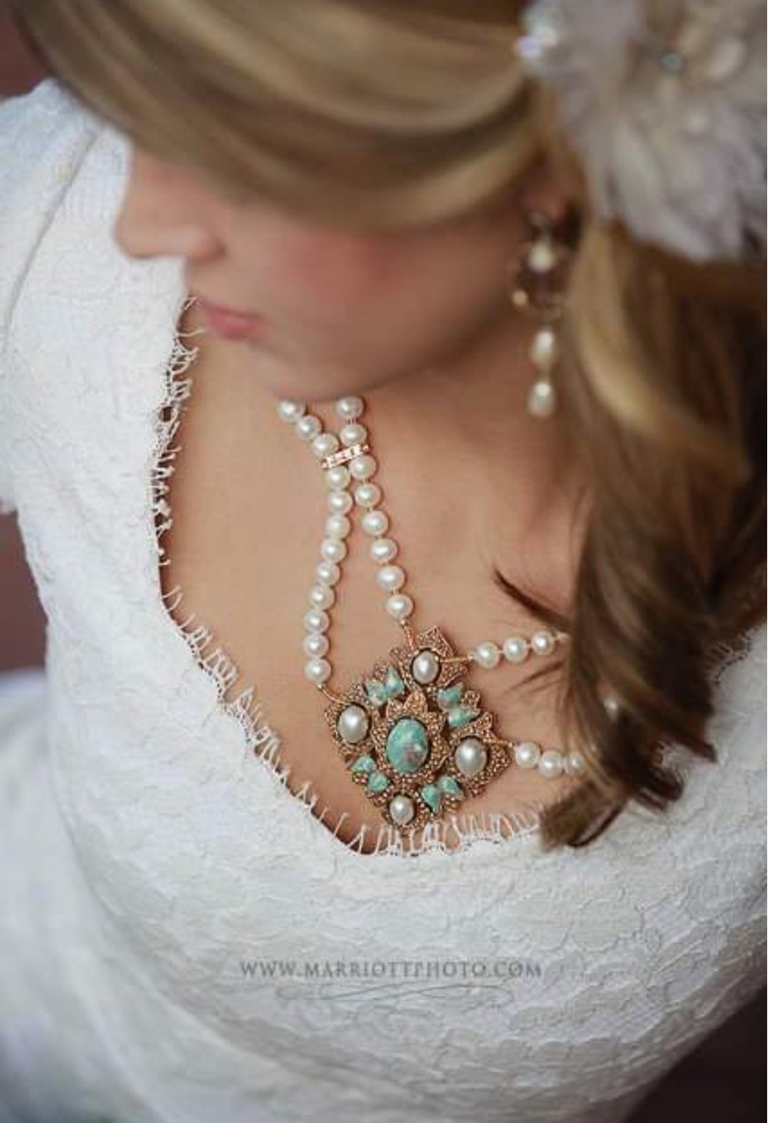 Close-up of a woman wearing pearl and turquoise jewelry, including a necklace and earrings, with her face partially visible and wearing a white textured dress.