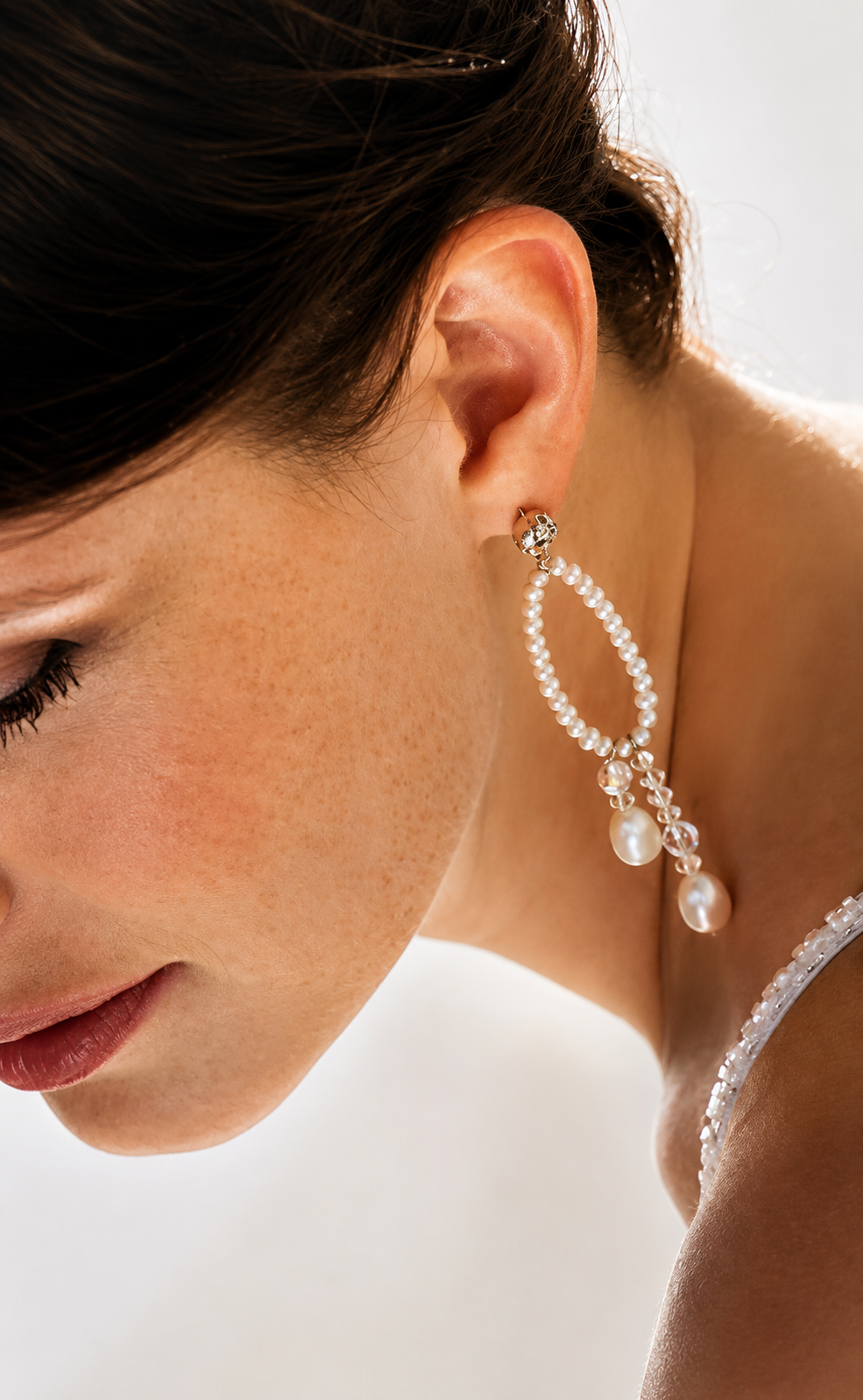 Close-up of a woman's face and neck with an elegant pearl and crystal earring.