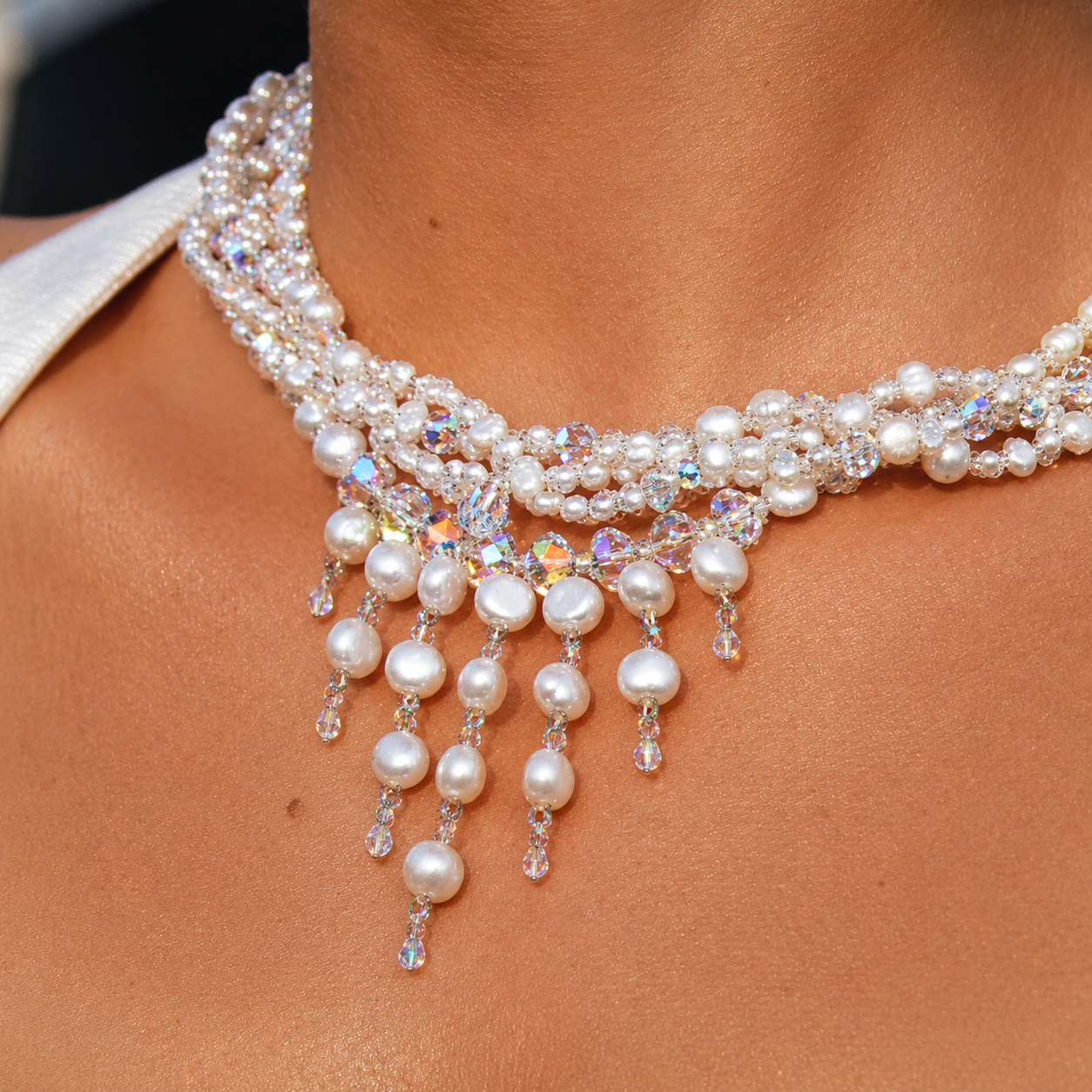 Close-up of a person's neck wearing a layered pearl and iridescent crystal necklace with dangling pearl and crystal beads.
