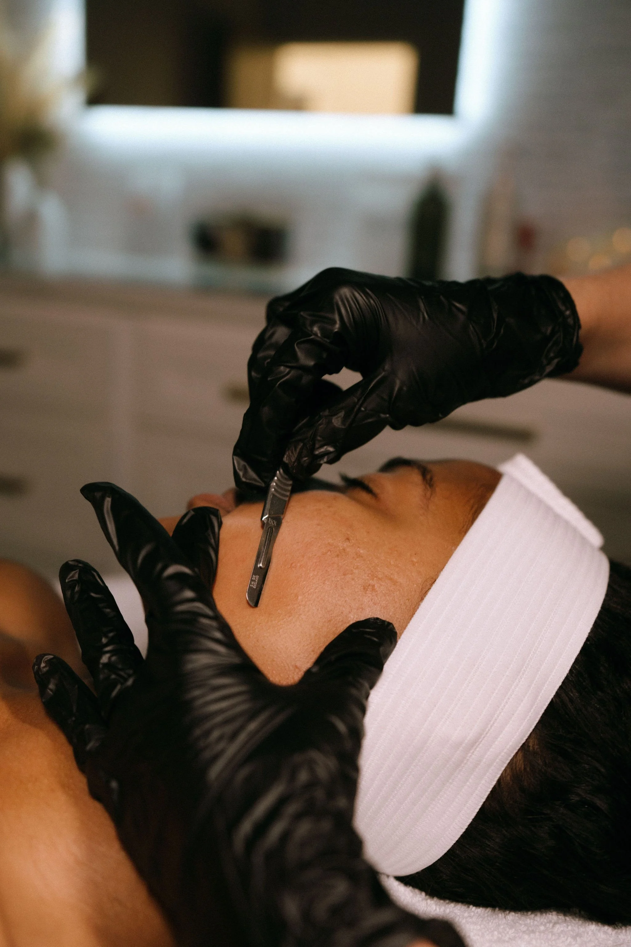 A person in a spa setting receives a dermaplane while lying on a treatment bed.