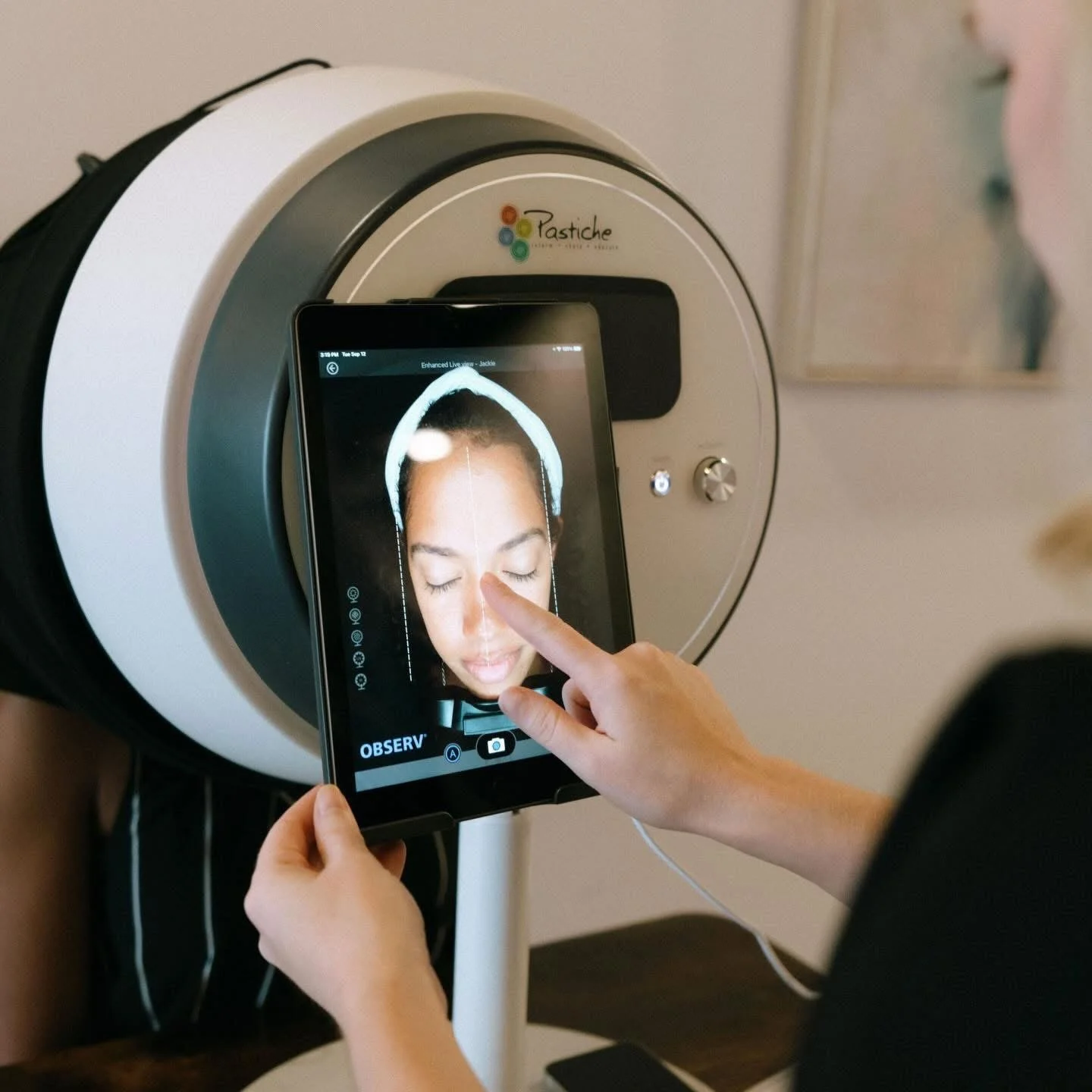 A person using a tablet to take a facial scan in a medical or spa machine labeled 'Pastiche'.