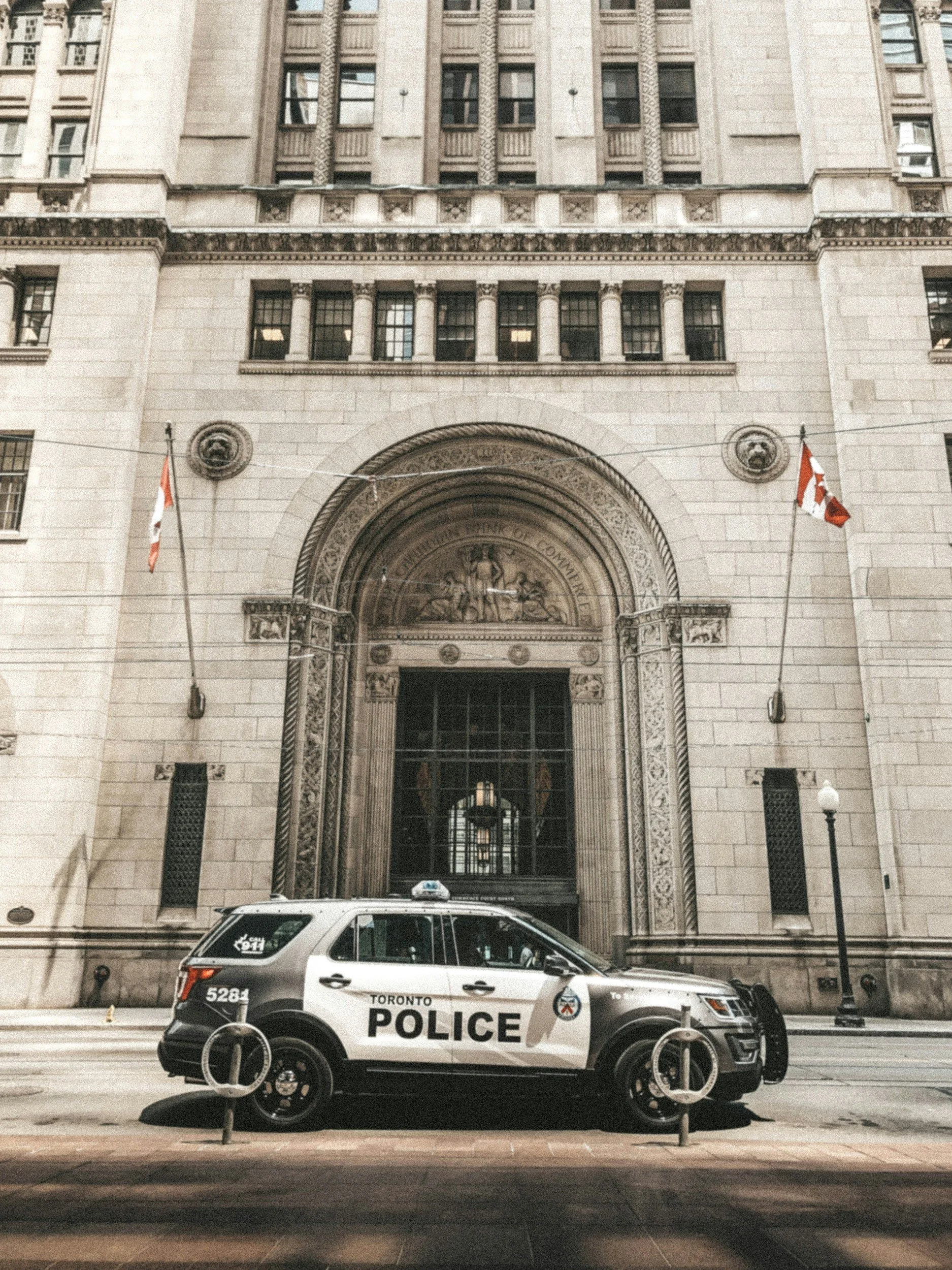 A Toronto police vehicle parked in front of a historic building with an ornate entrance, flags, and a large archway.