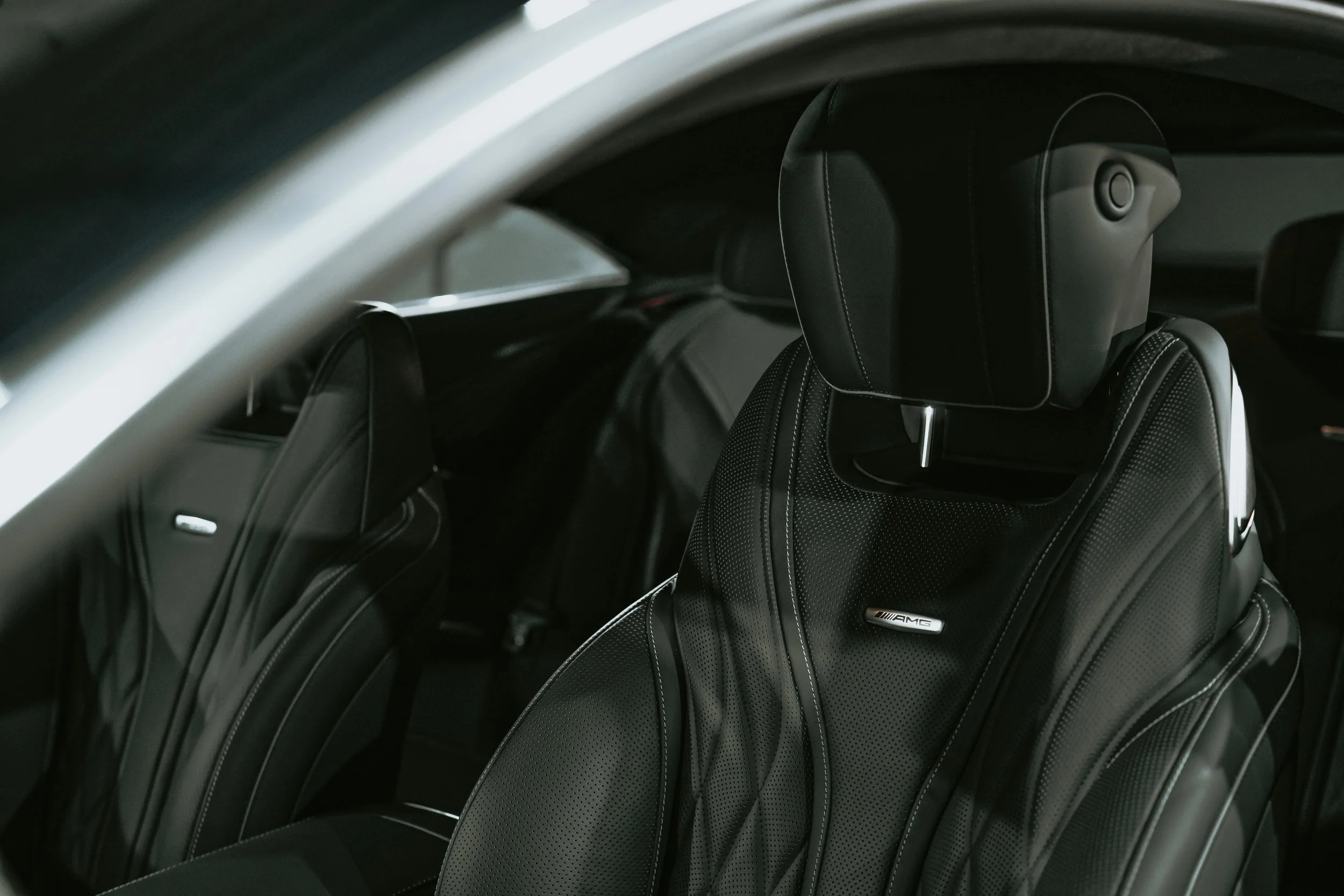 Interior of a luxury car, showing black leather seats with white stitching and a headrest with AMG logo.