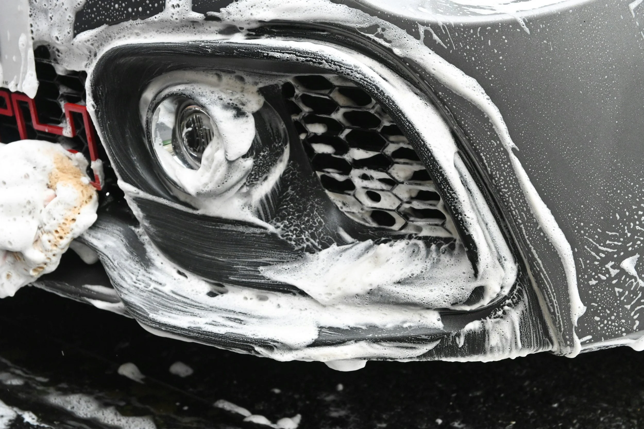 Close-up of a black car's front grille covered in soap suds during a car wash.