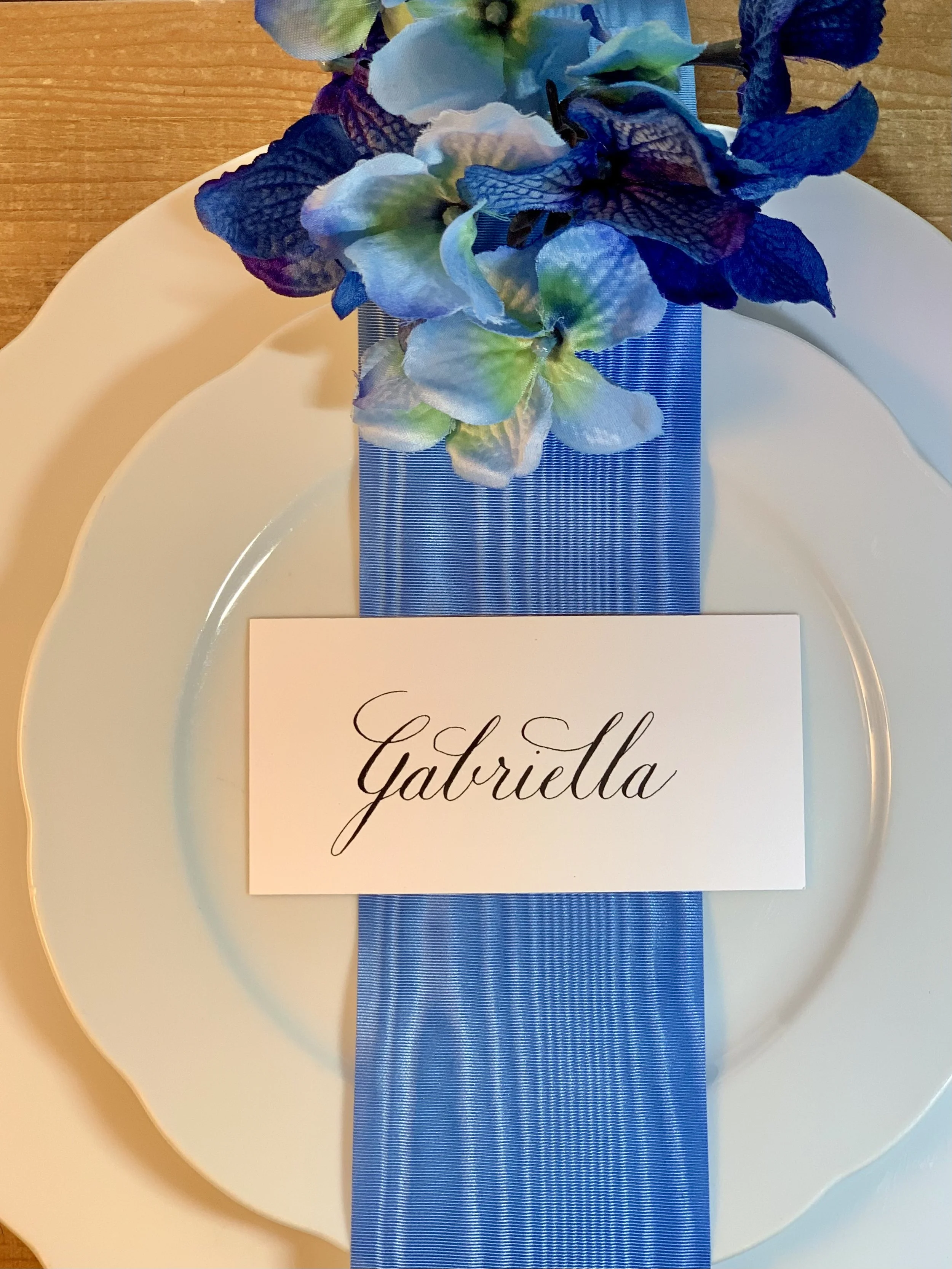 Calligraphy place card with black ink name shown at table setting at wedding or event.