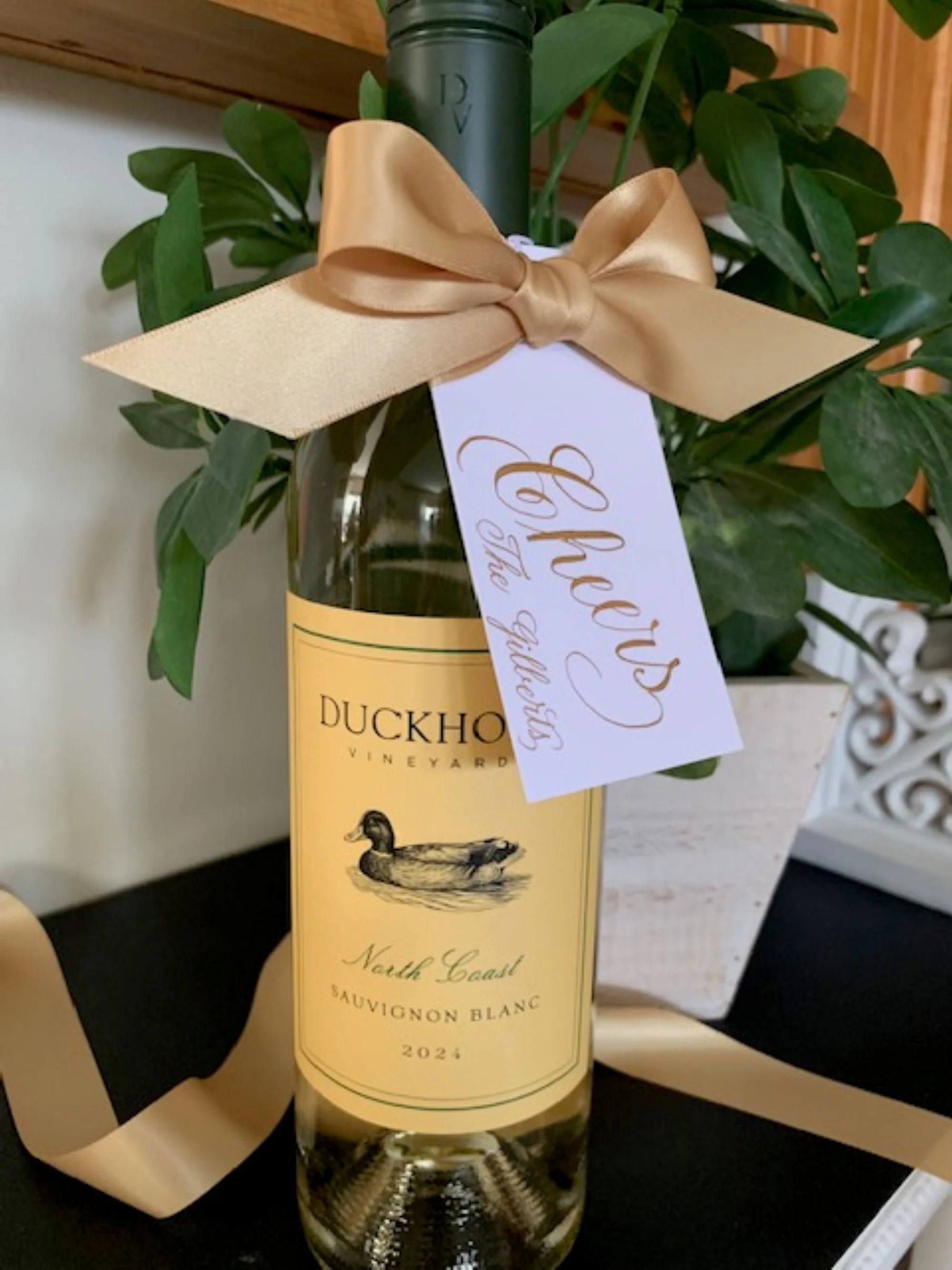 Cheers bottle gift tag handwritten in gold calligraphy and customized with personal name or business name and decorated with gold satin bow.