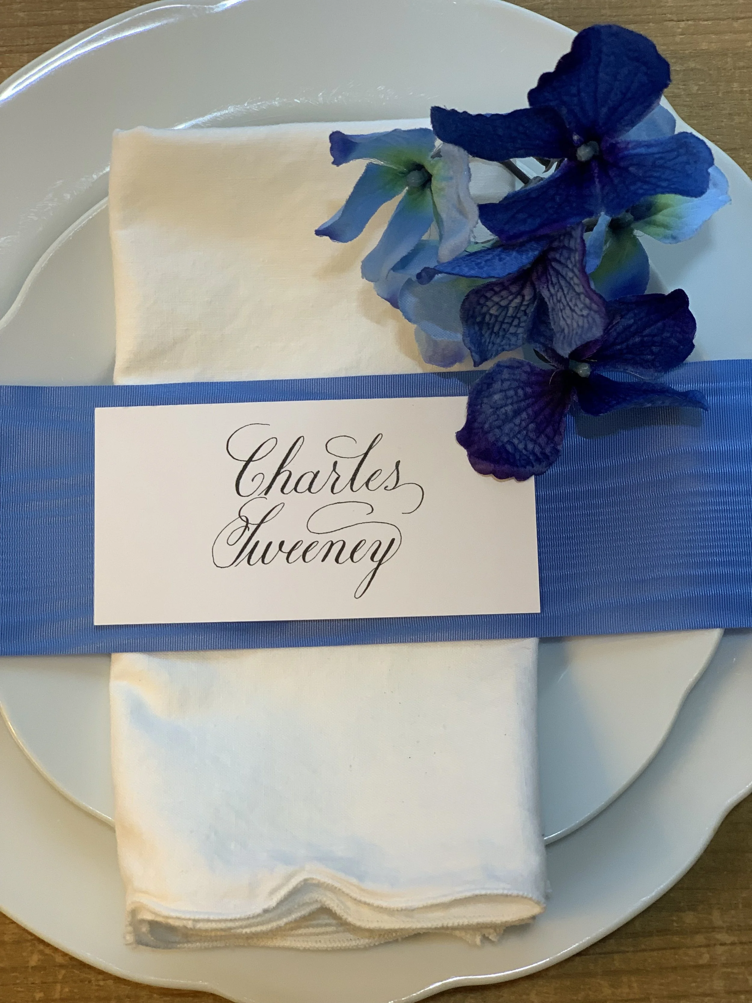 White placecard with customized handwritten calligraphy showing first and last name sitting on a plate at a wedding place setting.