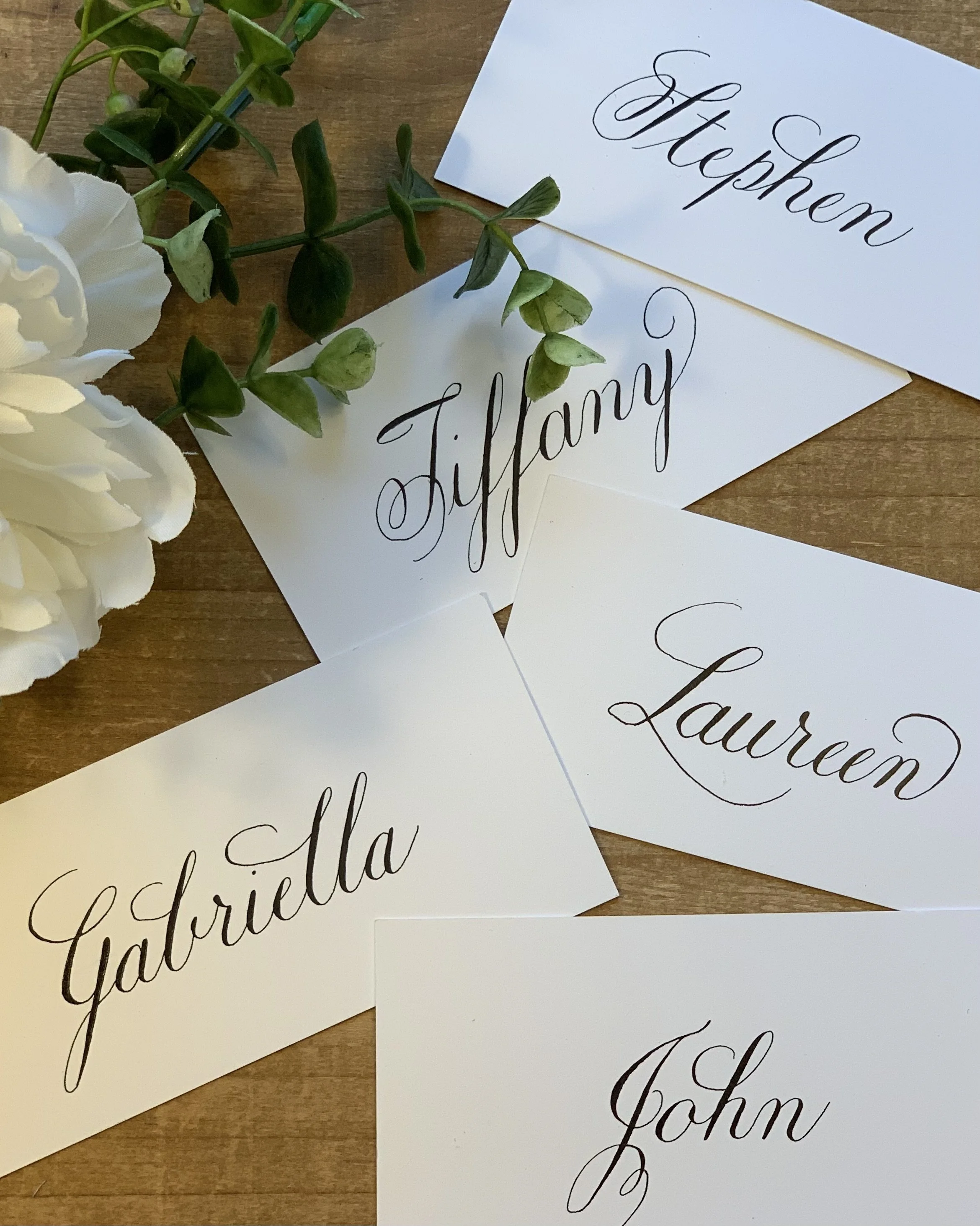 Handwritten custom calligraphy place cards showing first names in black ink laying on table.