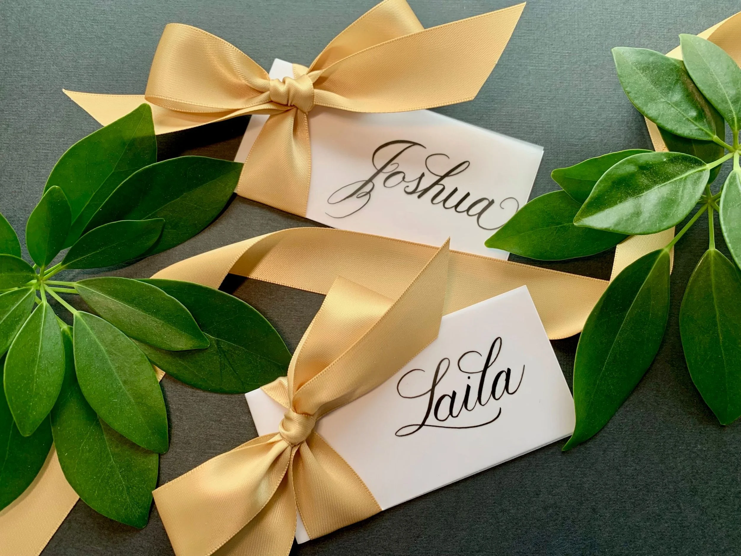Calligraphy gold ribbon and bow place cards with handwritten first names for wedding table