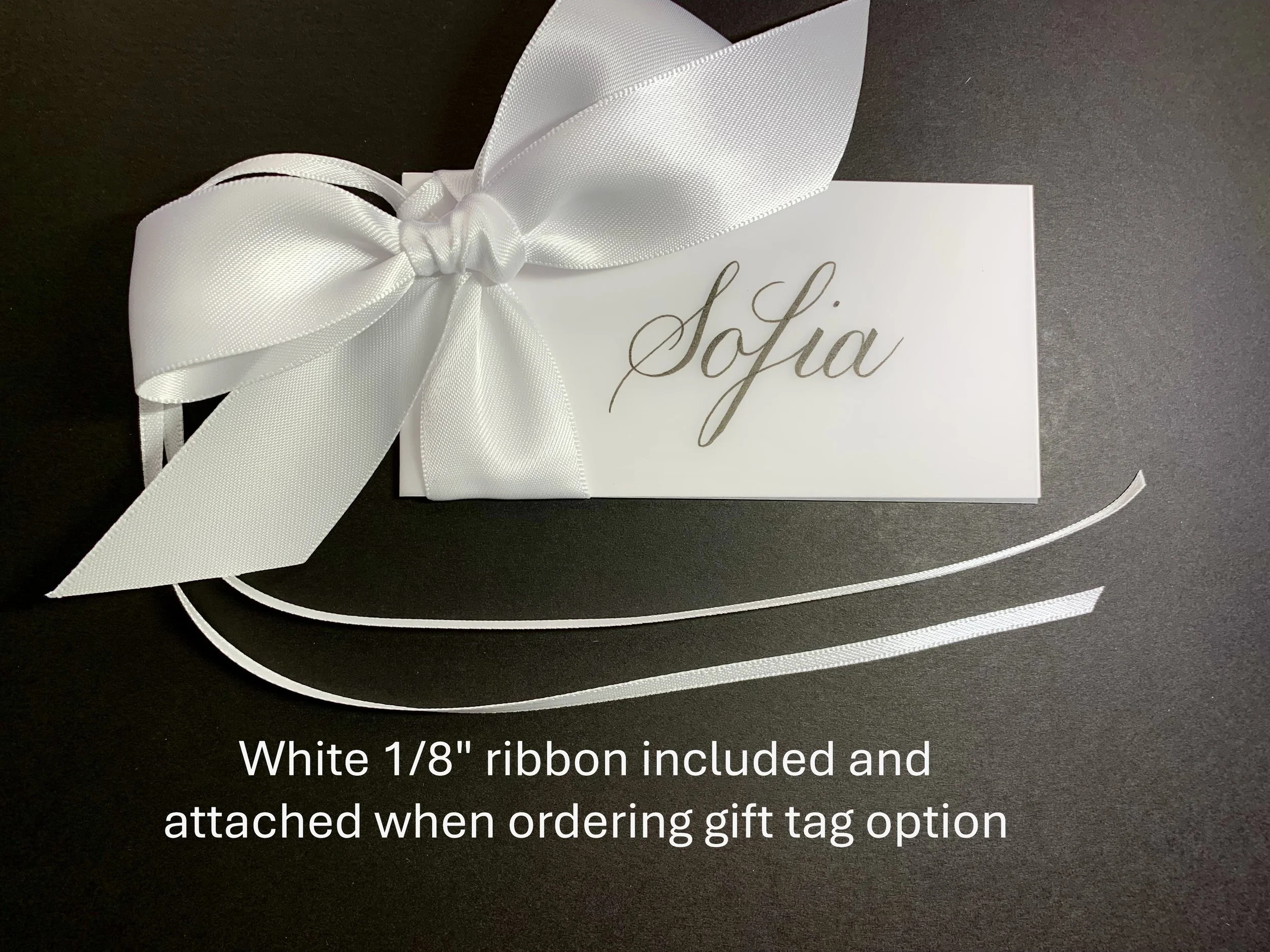 A white gift box decorated with a large satin ribbon tied into a bow on top, placed on a dark surface.