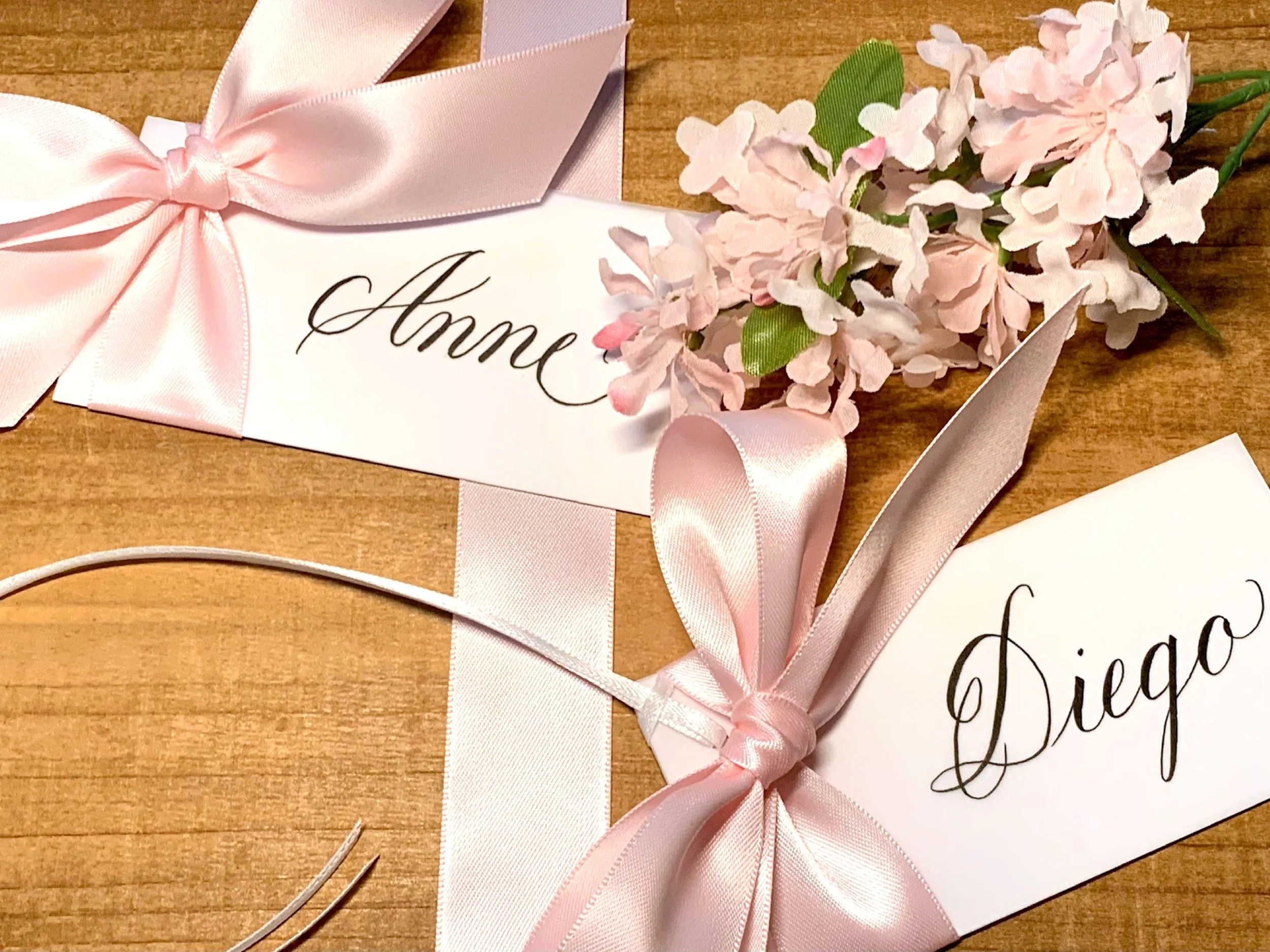 Custom calligraphy white place cards and attached pink satin ribbon tied in a bow.